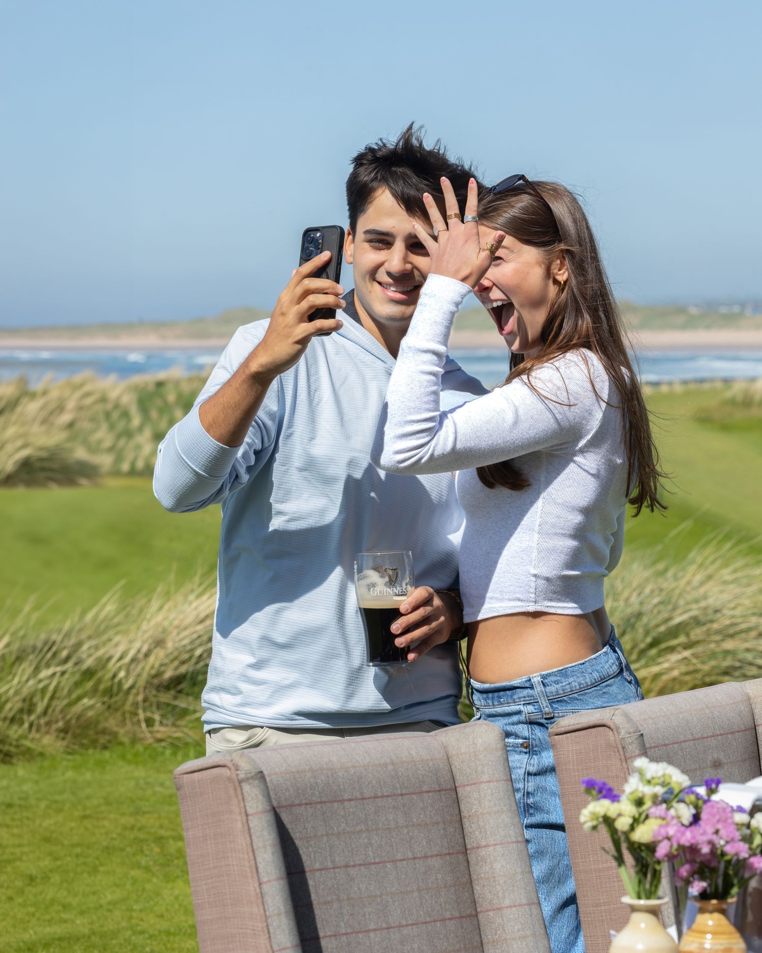 A couple laughing and taking a selfie outdoors after their proposal in Doonbeg, Co Clare, Ireland