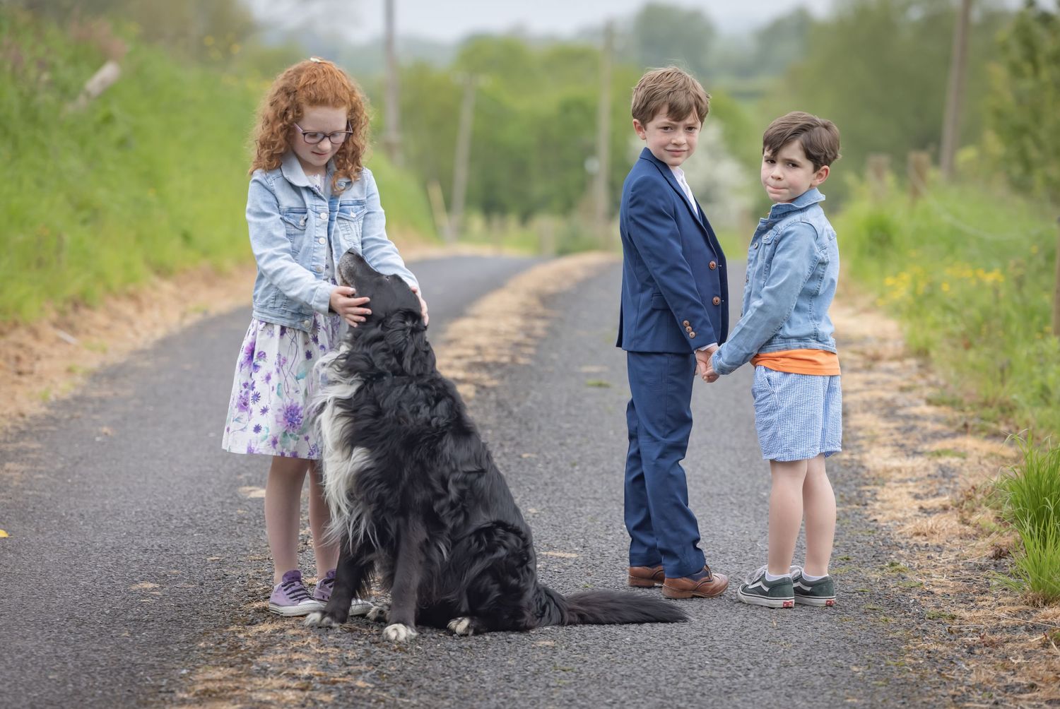 Children and a large black shaggy dog interact on a countryside path on a sunny spring day.