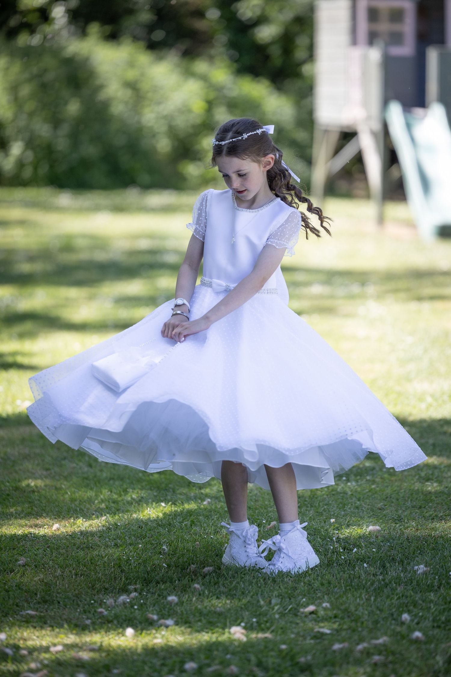 A person in a white dress and sneakers walks across a sunny green lawn with daisies.