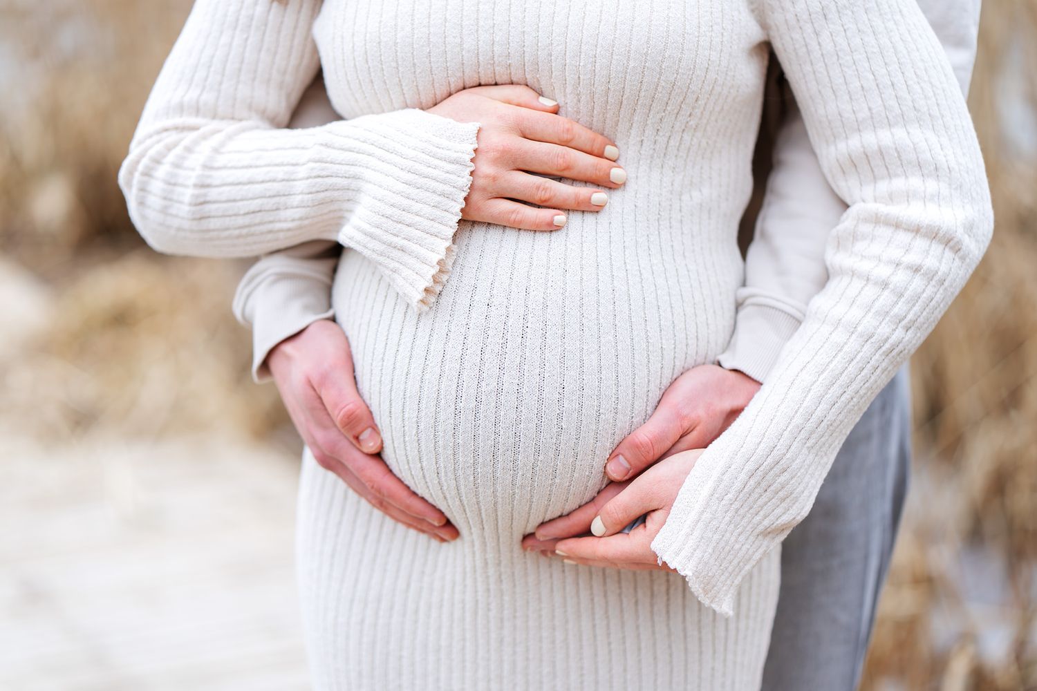 Hands gently cradling a pregnant belly in a white knit sweater.