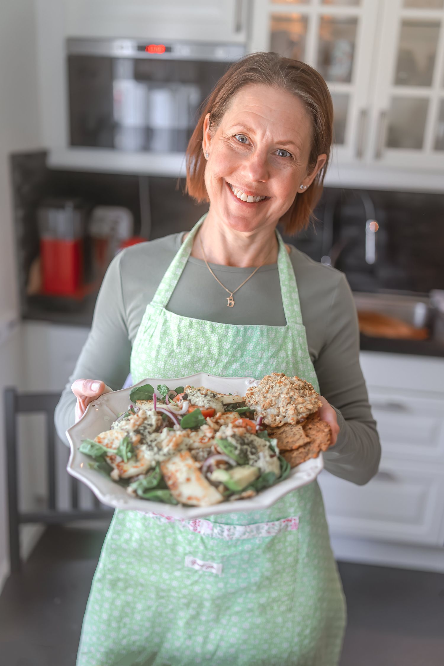 Person wearing mint green apron presenting a fresh homemade meal in modern kitchen.