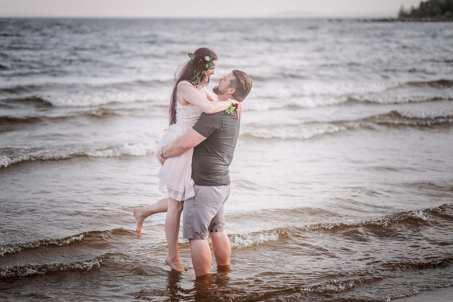 Couple embracing while standing in shallow ocean water at sunset.