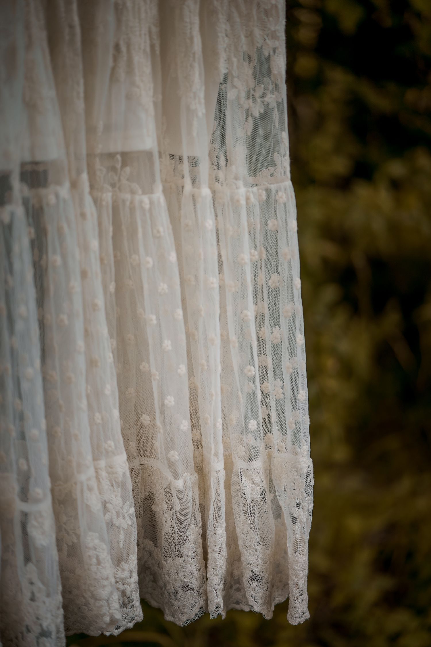 A close-up view of delicate white lace curtains with intricate floral patterns against a dark background.