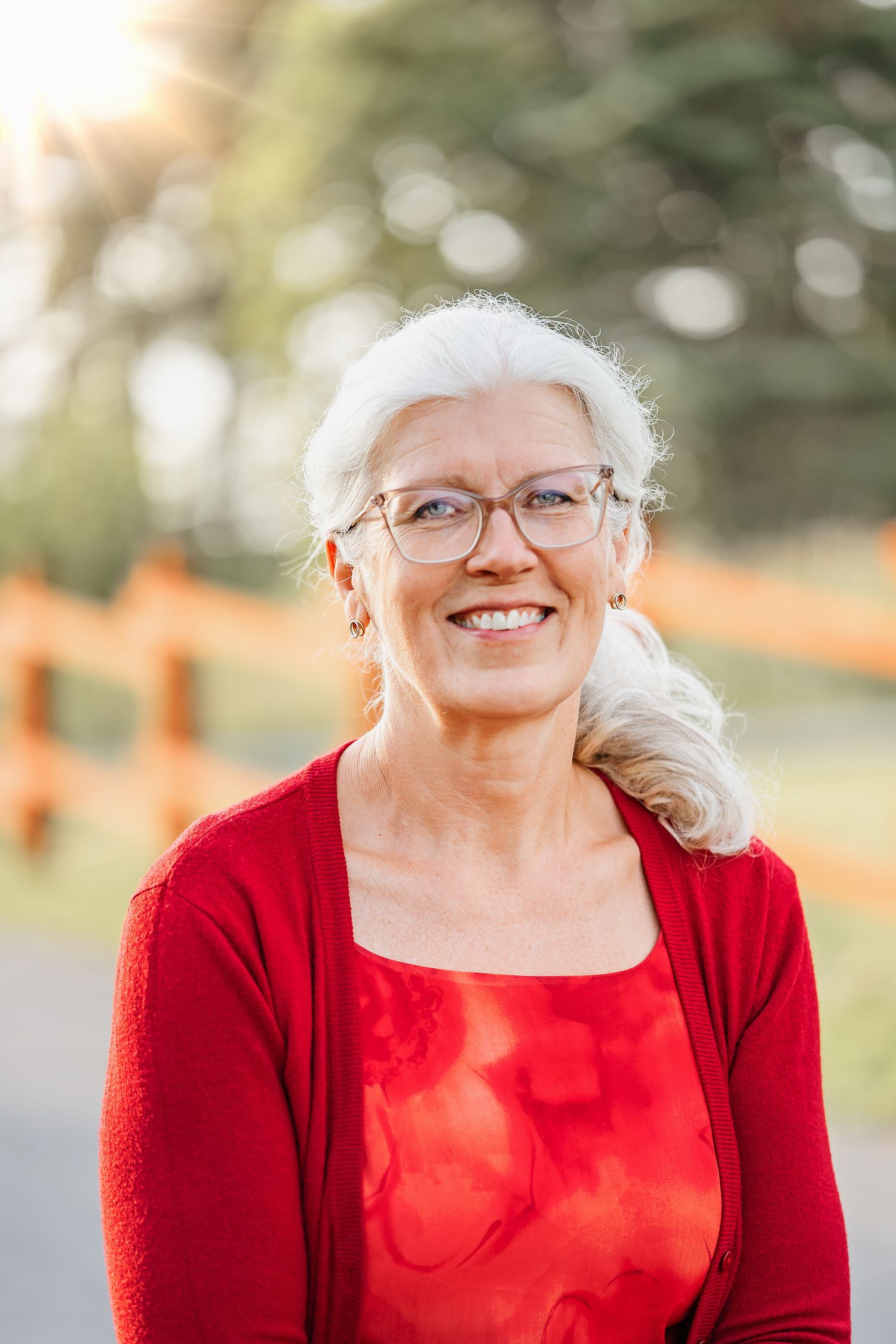Person wearing red cardigan and glasses outdoors with natural bokeh background.