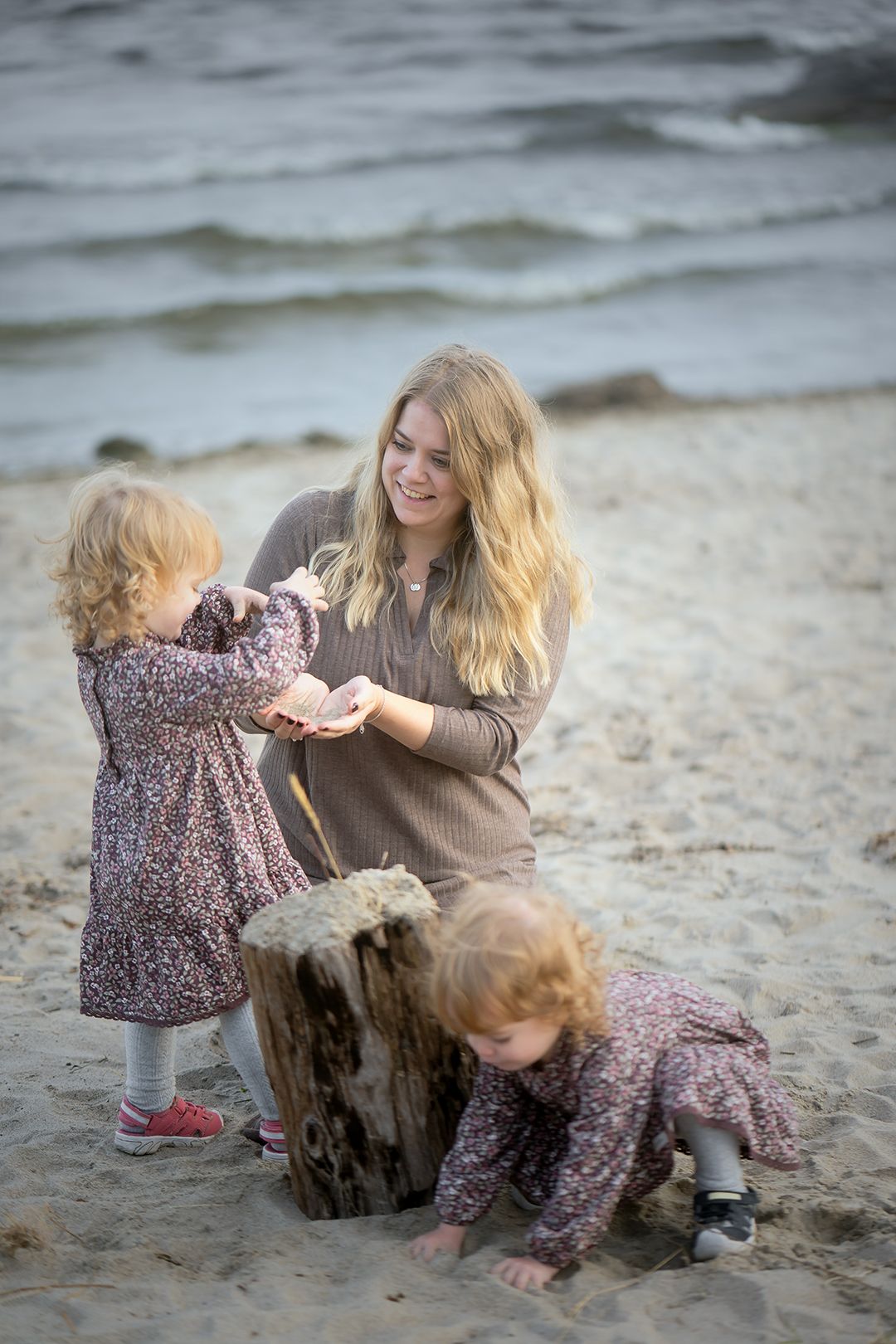Candid beach scene with playful children in floral dresses exploring by a driftwood log.