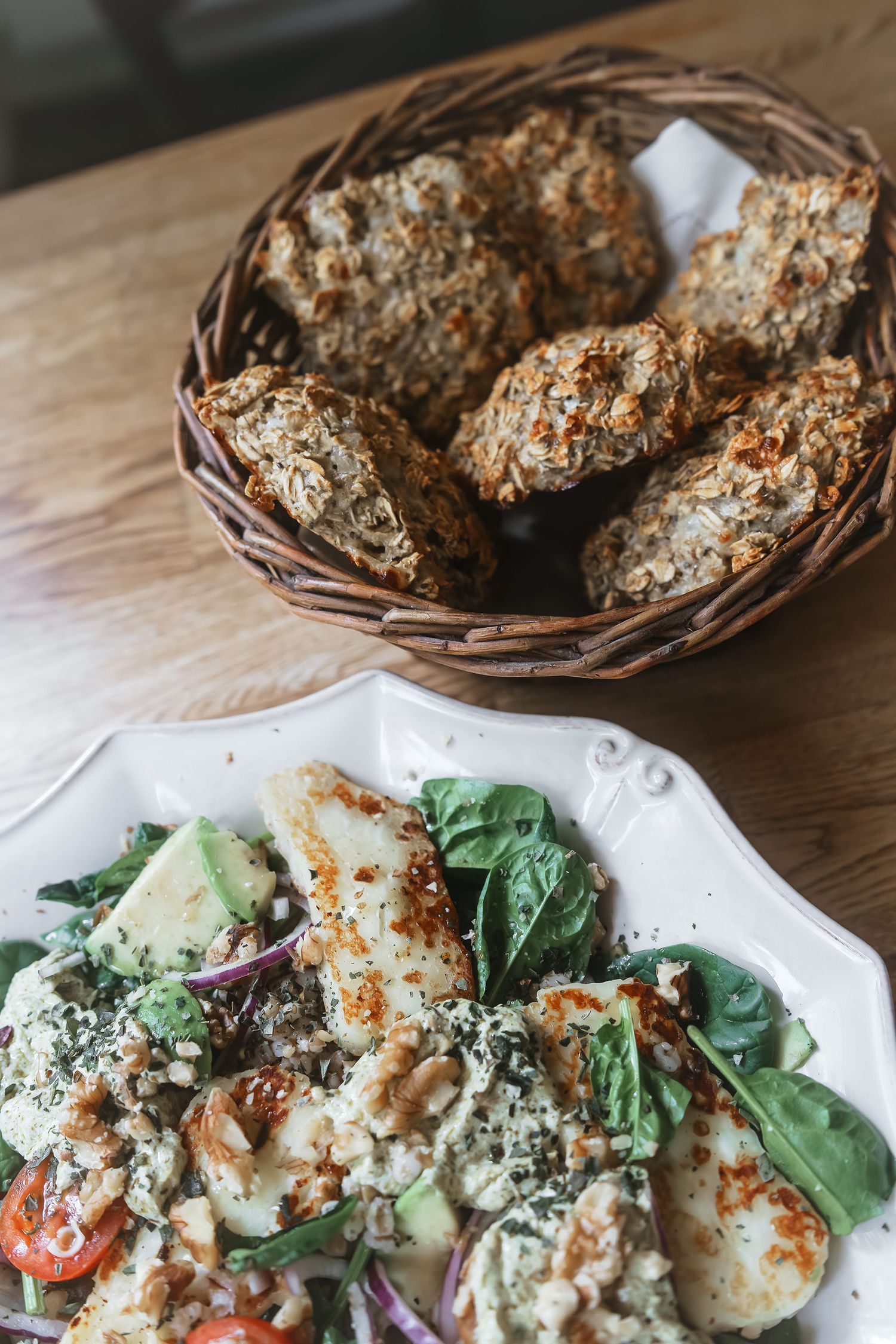 A fresh salad with grilled chicken and rustic bread basket on wooden table.