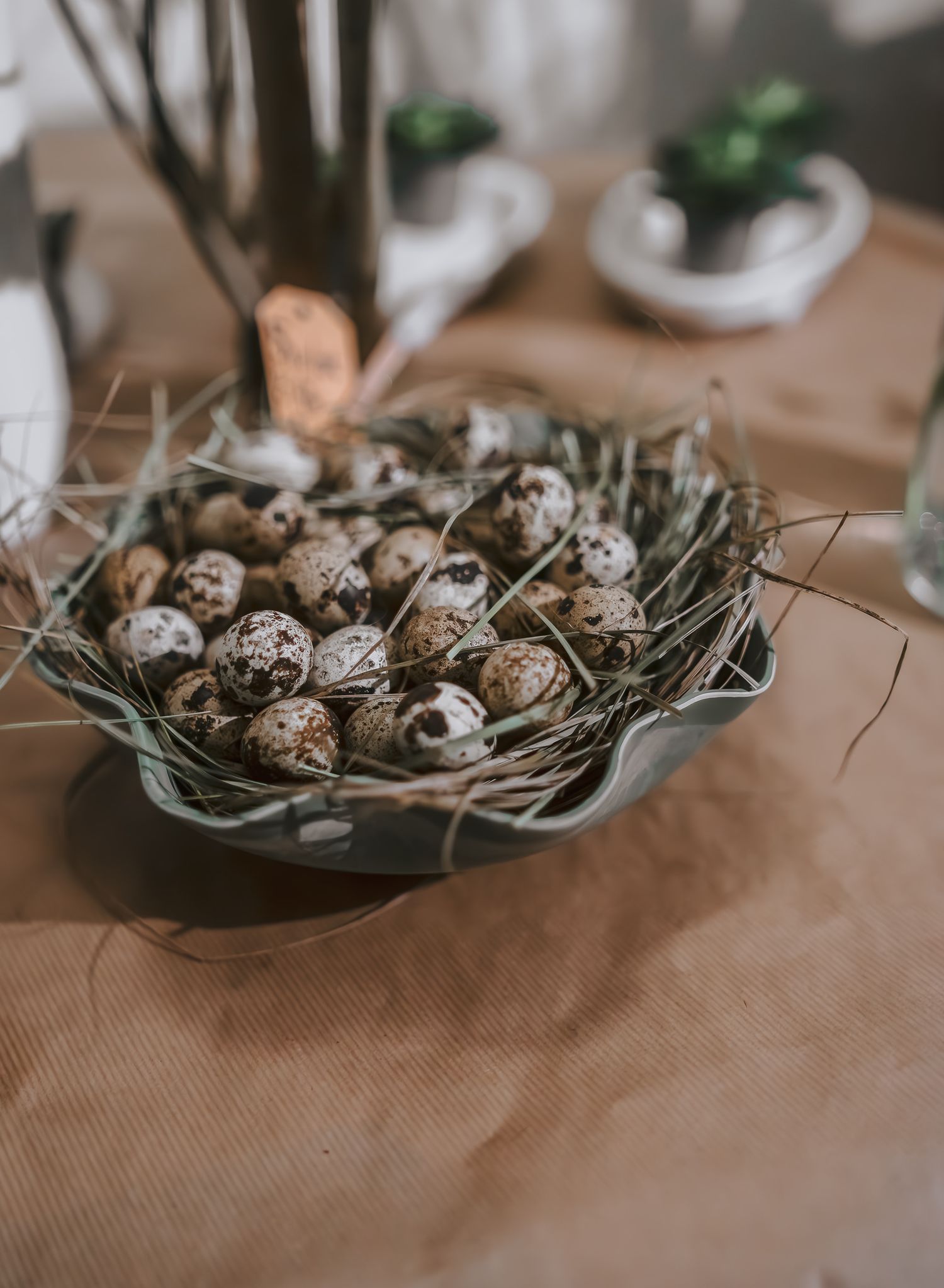 Decorative nest display with quail eggs and straw in a rustic bowl on brown surface.