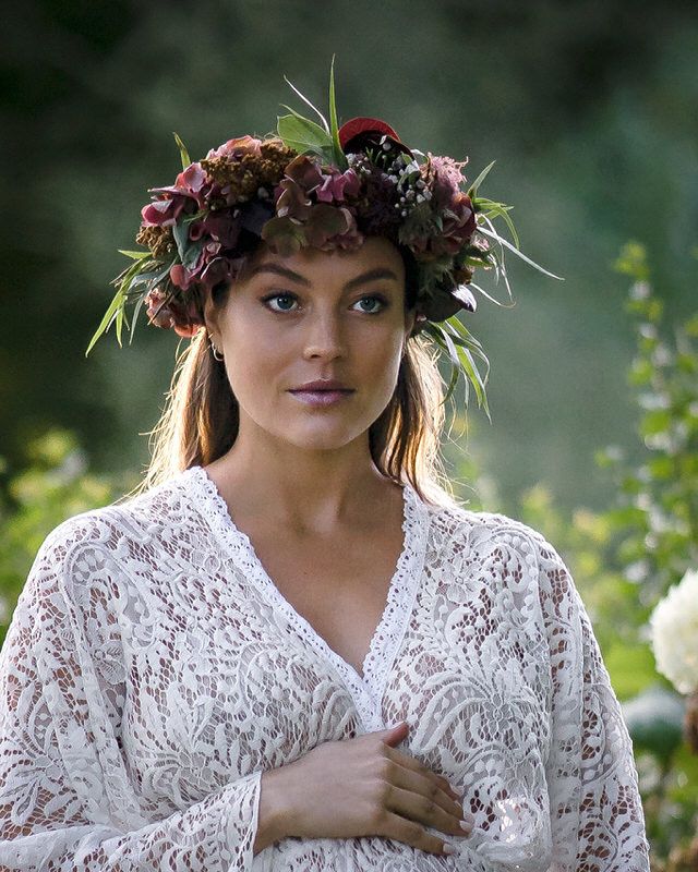 Portrait of woman in white lace dress wearing an elaborate floral crown in golden sunlight.