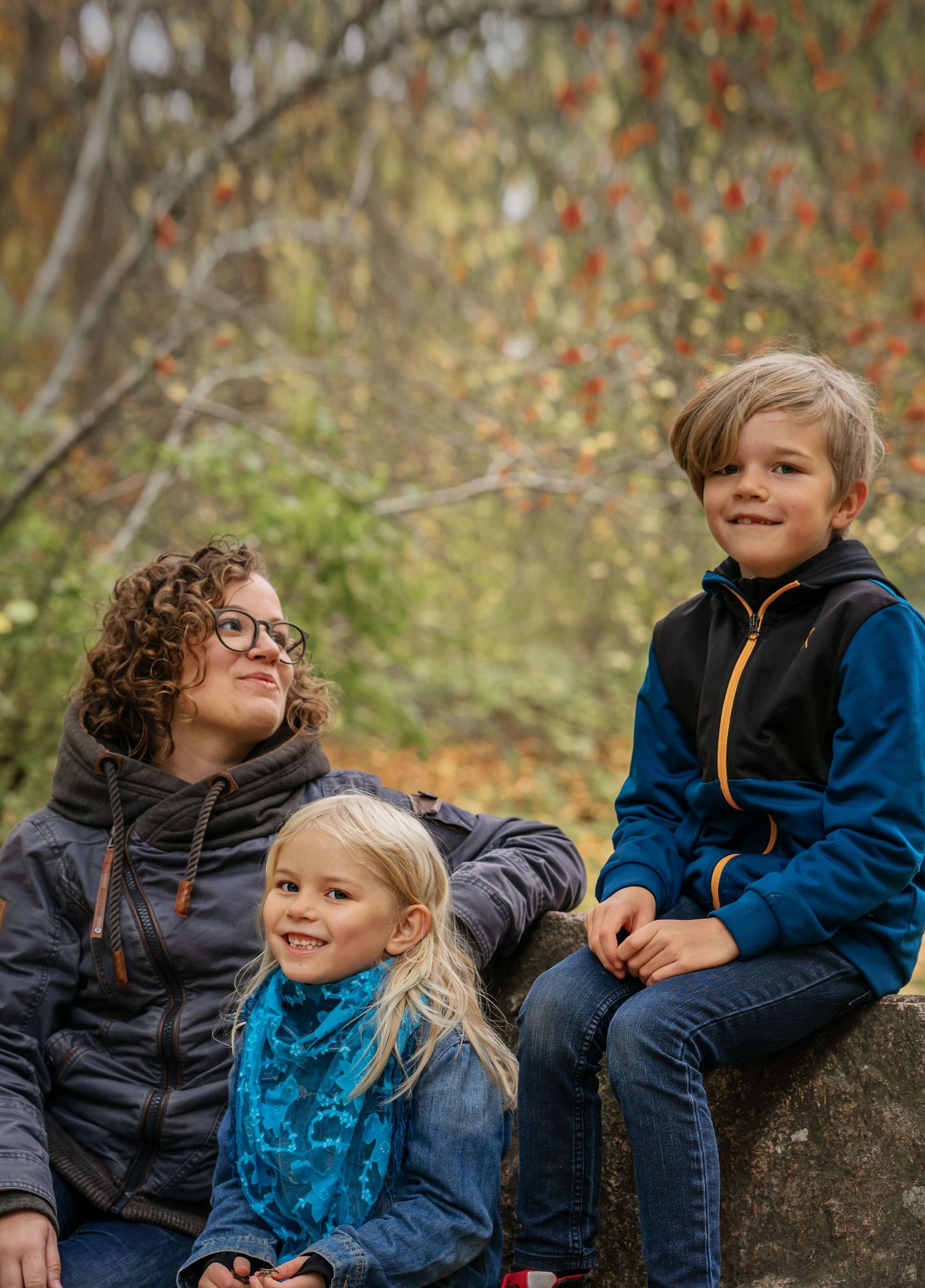 Family group sitting on rock together during autumn photoshoot with colorful fall foliage.