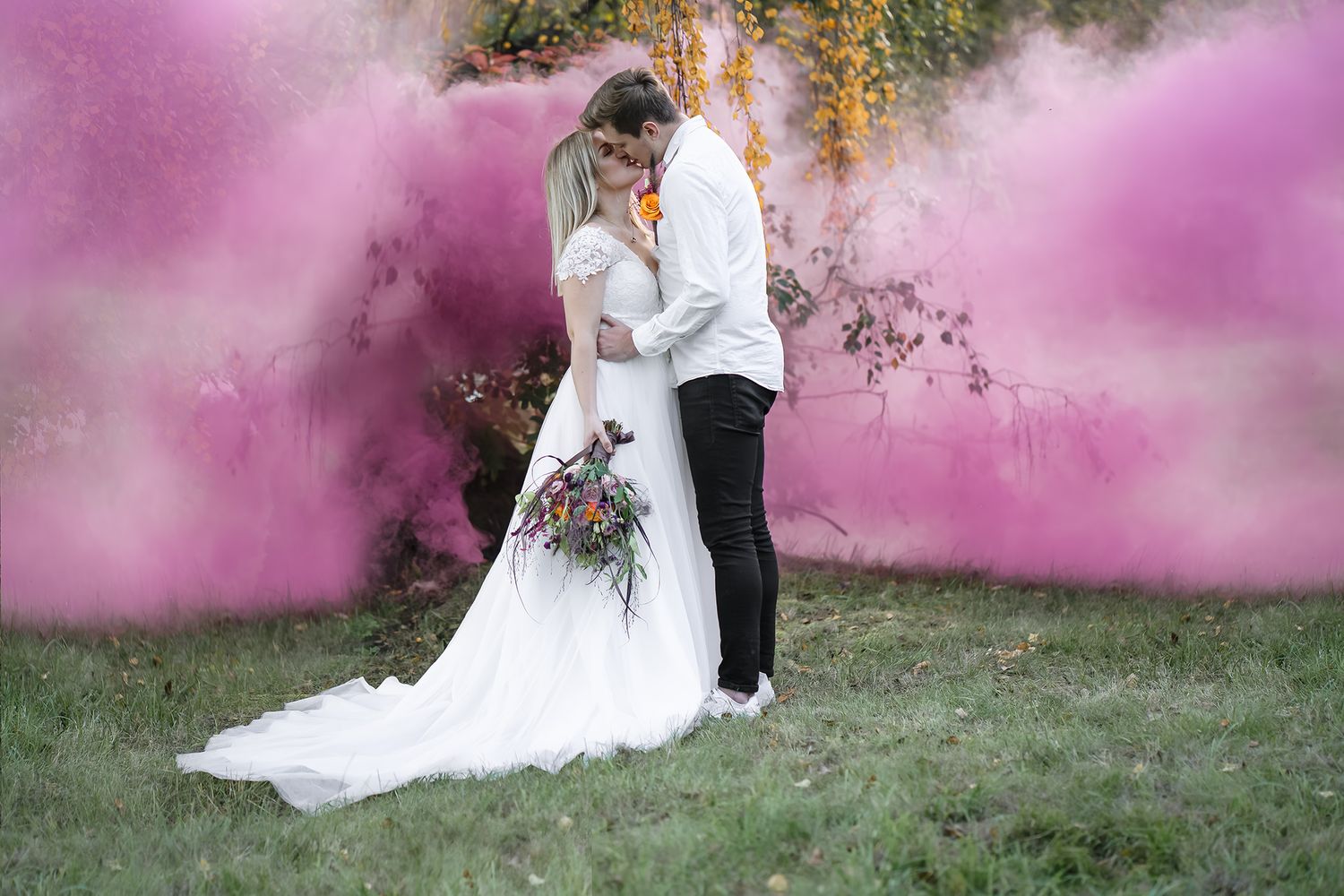 A wedding couple shares an intimate moment amid dramatic pink smoke effects in an outdoor setting.