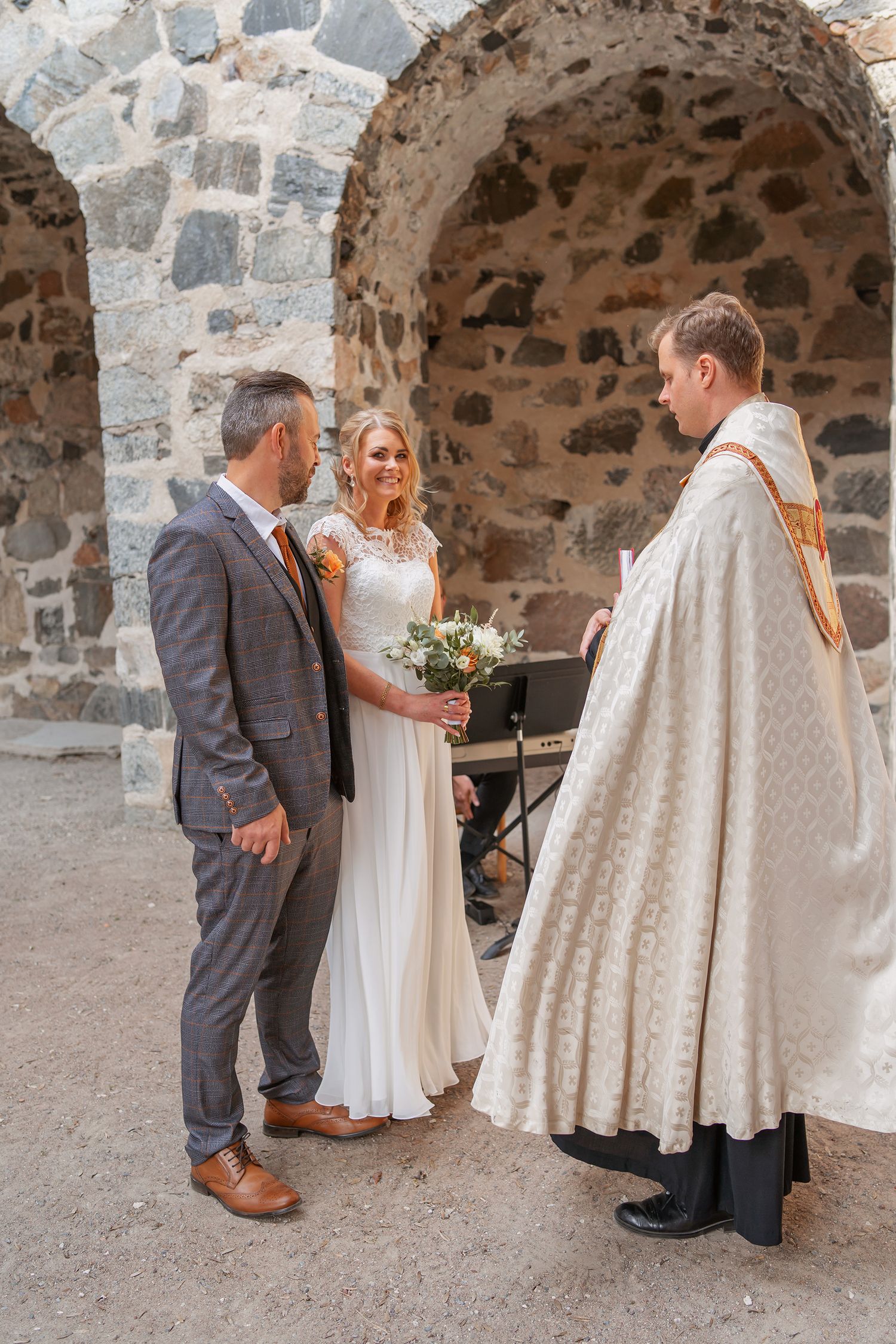 Wedding ceremony in a stone archway with priest officiating.