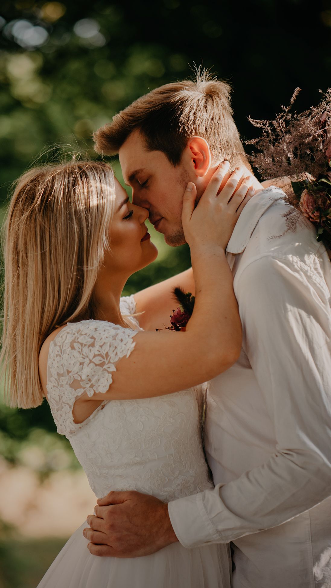 Intimate moment between newlyweds sharing a romantic kiss outdoors.