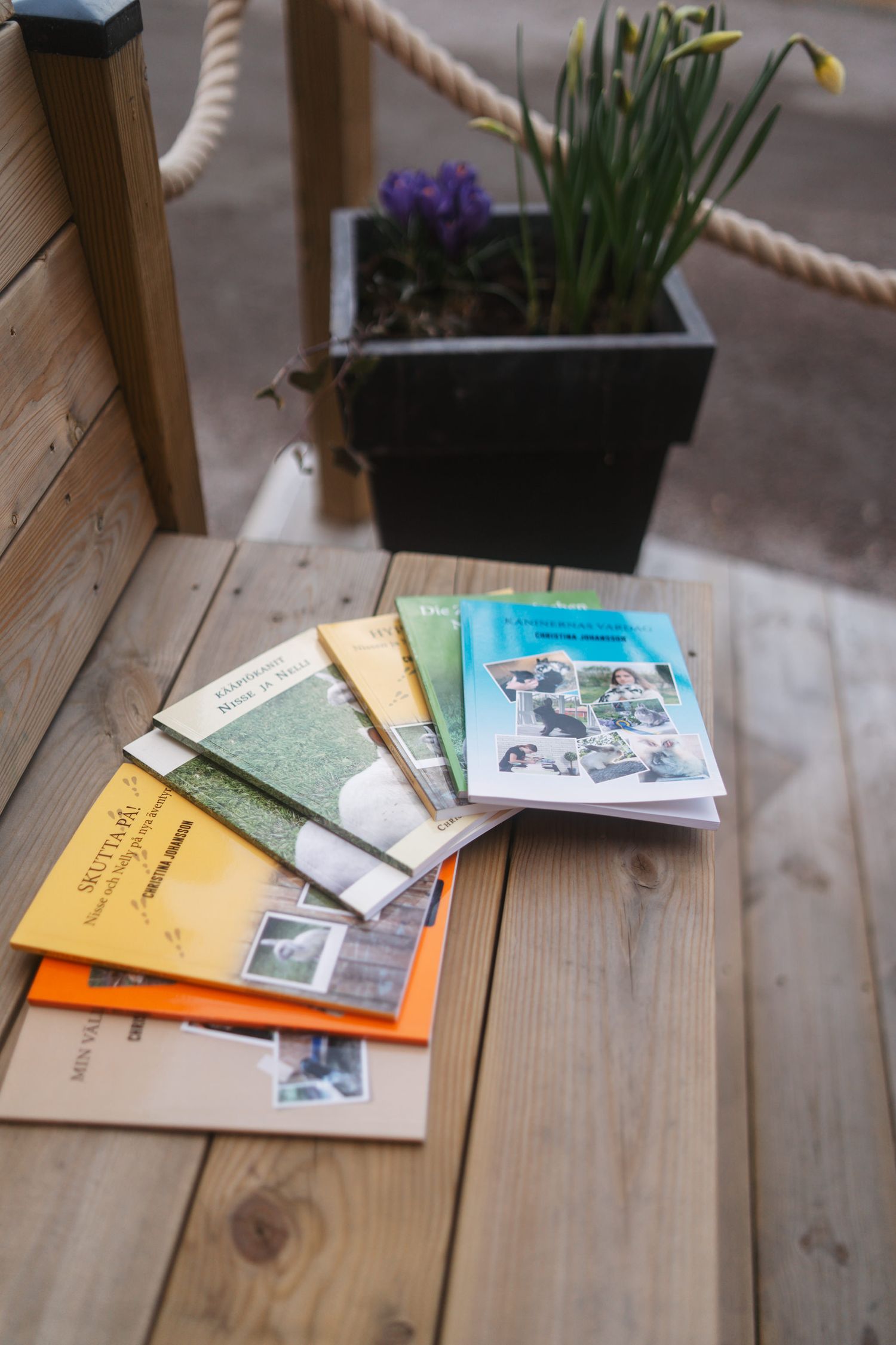 Books and printed materials are arranged on a wooden surface with potted plants in the background.