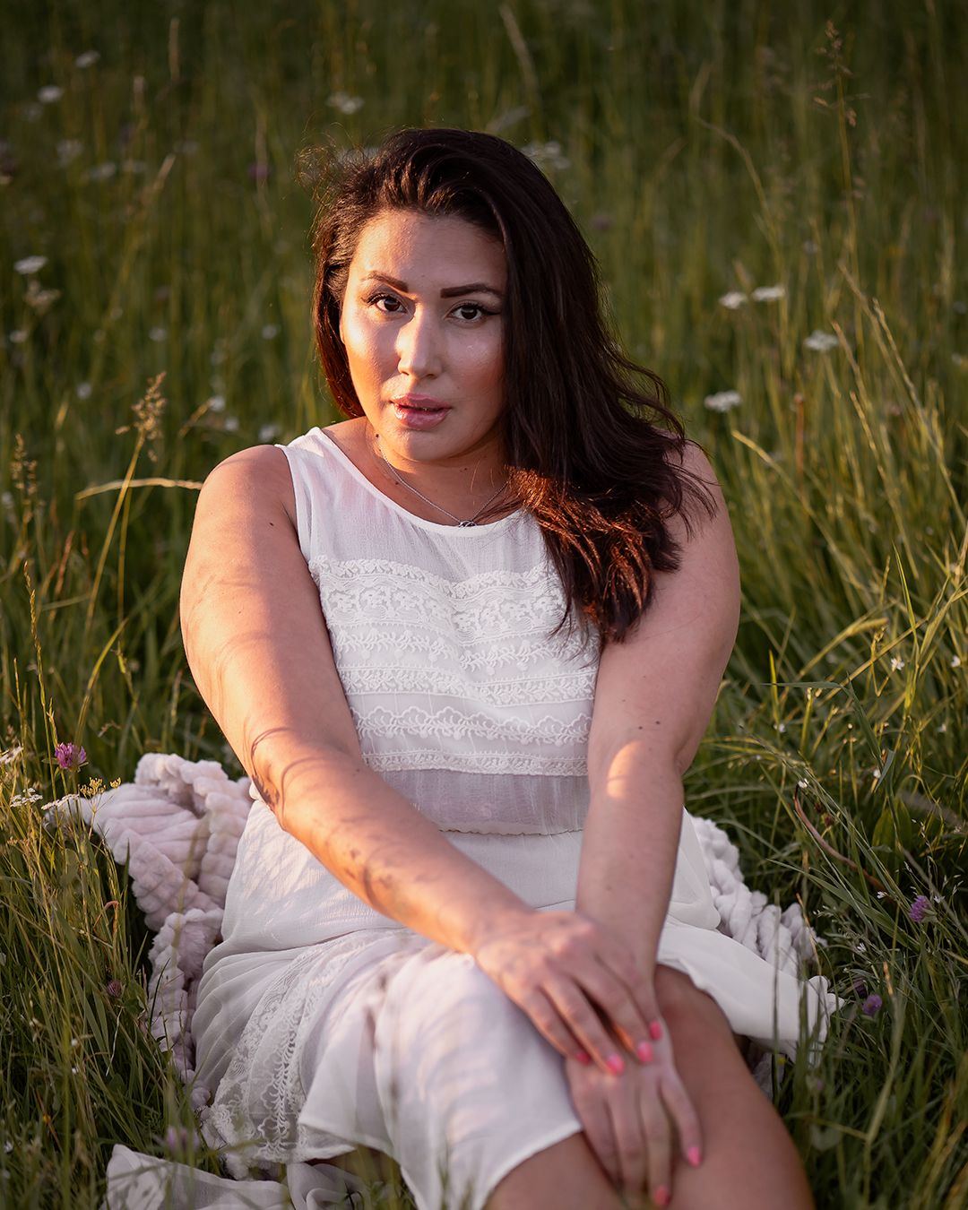 Portrait of person in white dress sitting among tall grass at golden hour.