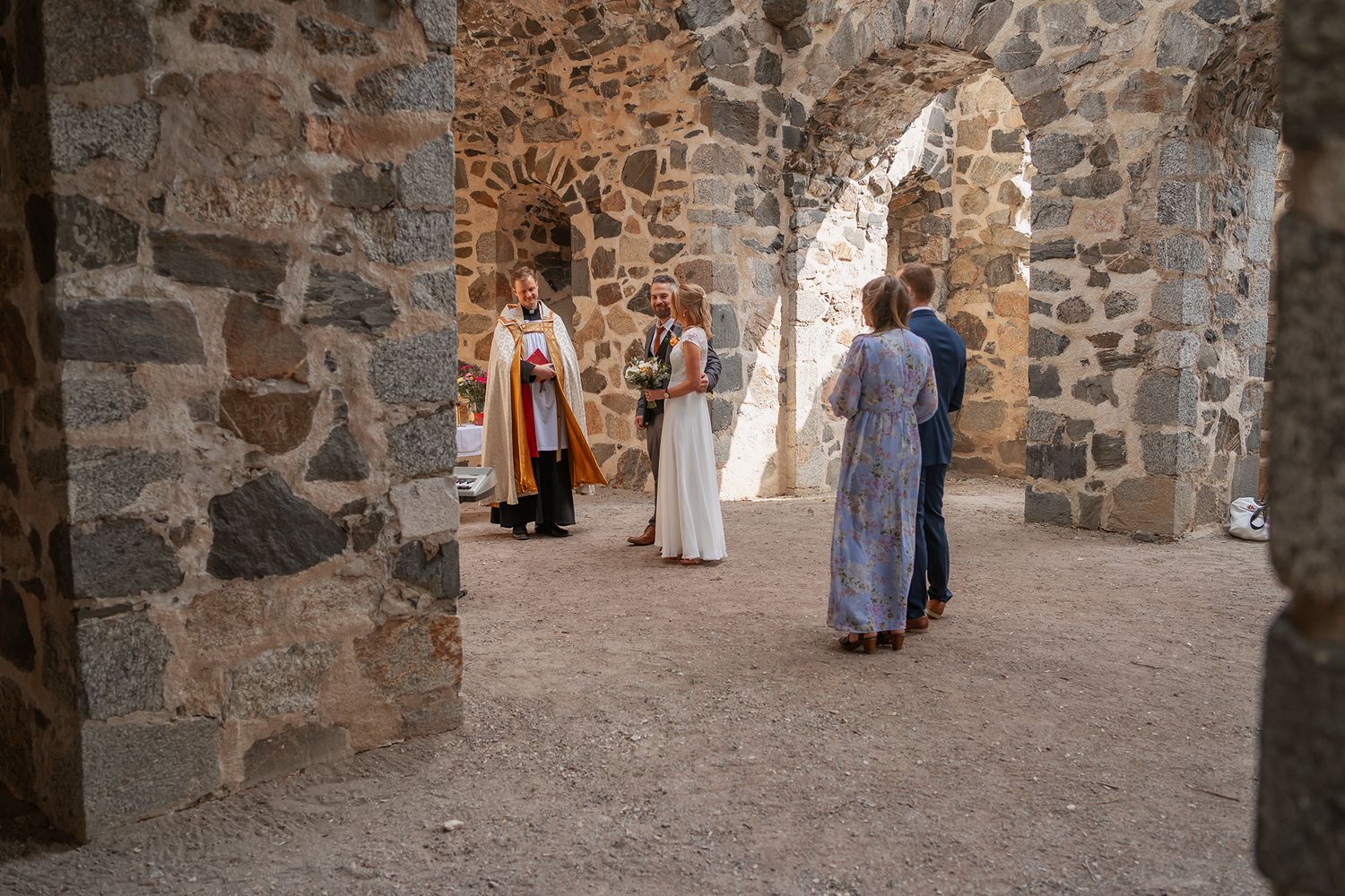 Wedding guests and clergy gathered in historic stone ruins.