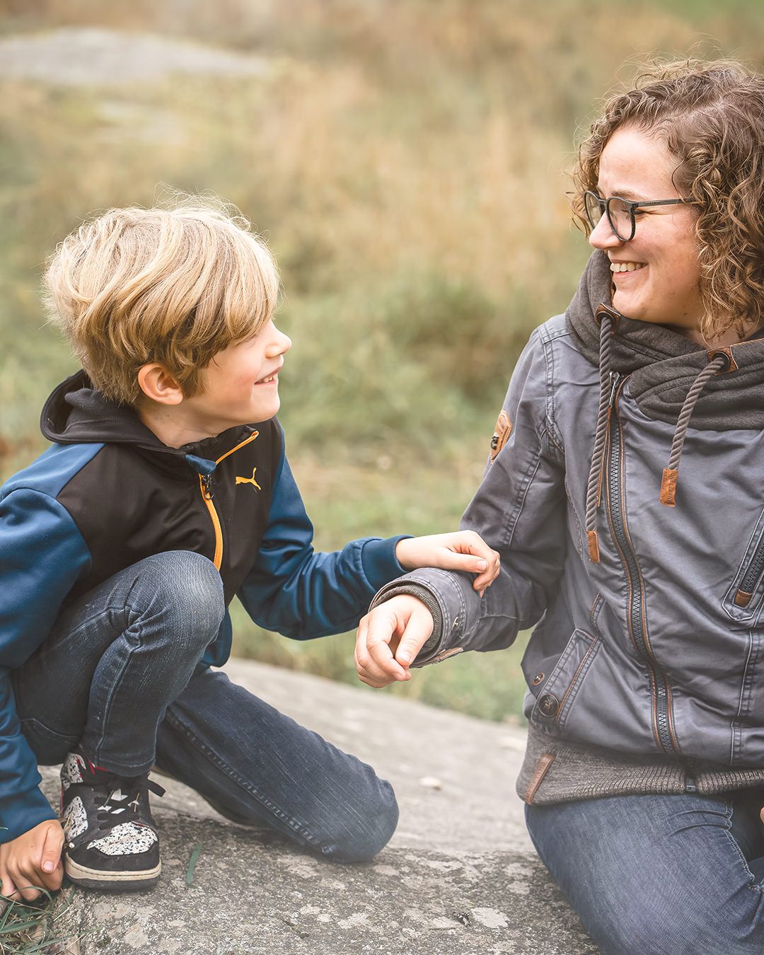 A candid outdoor interaction between a youth and an adult smiling and sitting together in casual attire.