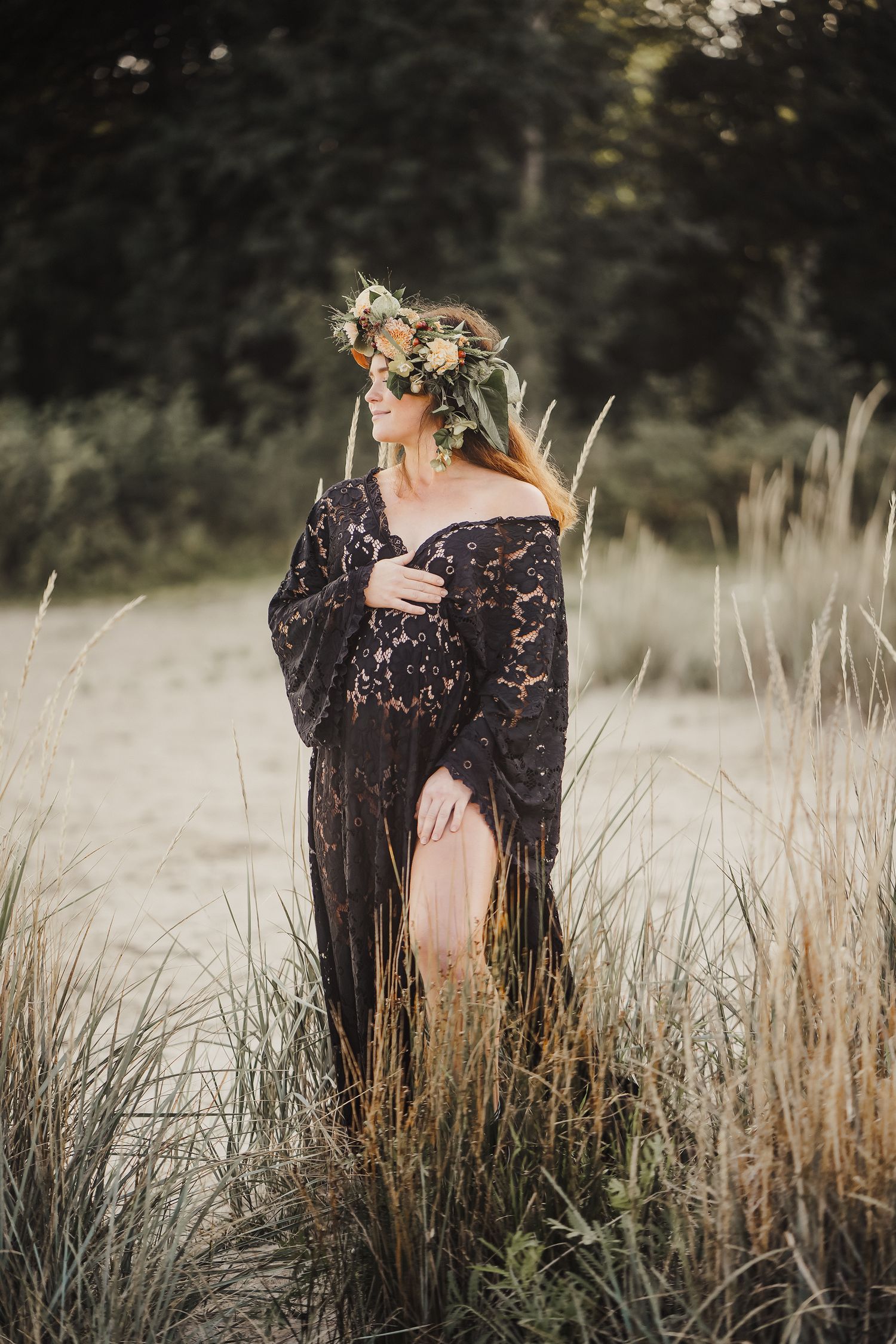 Ethereal portrait in tall grass shows figure wearing black lace dress and floral crown against moody natural backdrop.