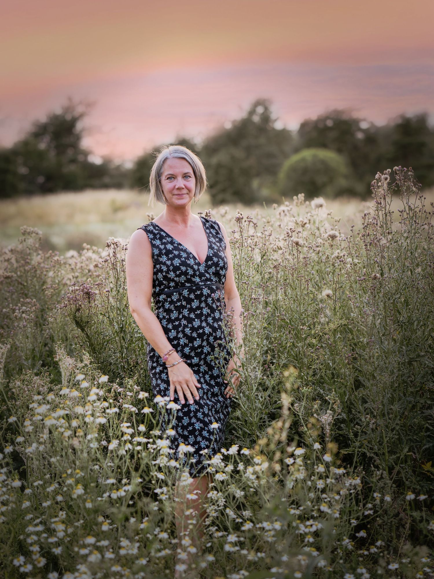 A person in a floral dress stands in a wildflower meadow at sunset creating a dreamy summer portrait.