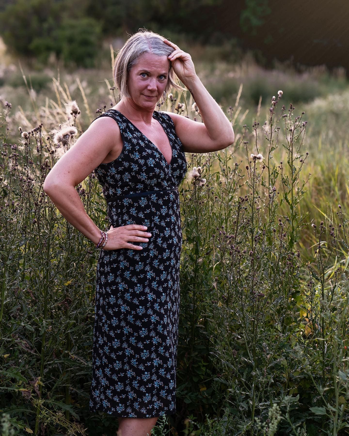 Summer portrait of person in floral dress standing in tall wildflower meadow at sunset.
