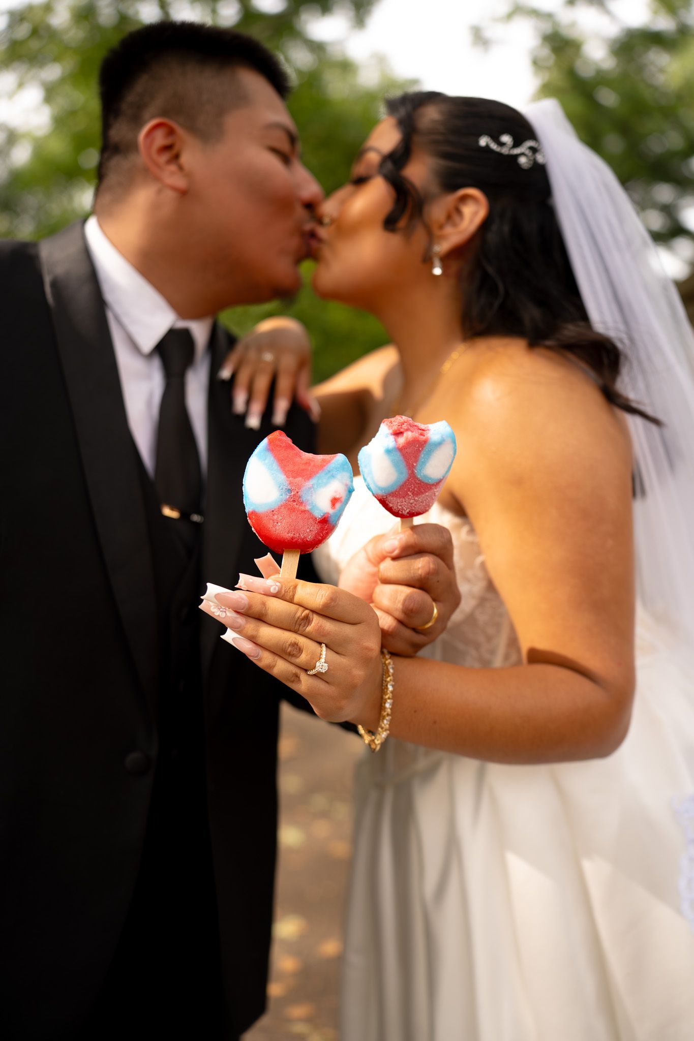 A wedding couple shares a sweet moment while holding colorful macarons in a garden setting.