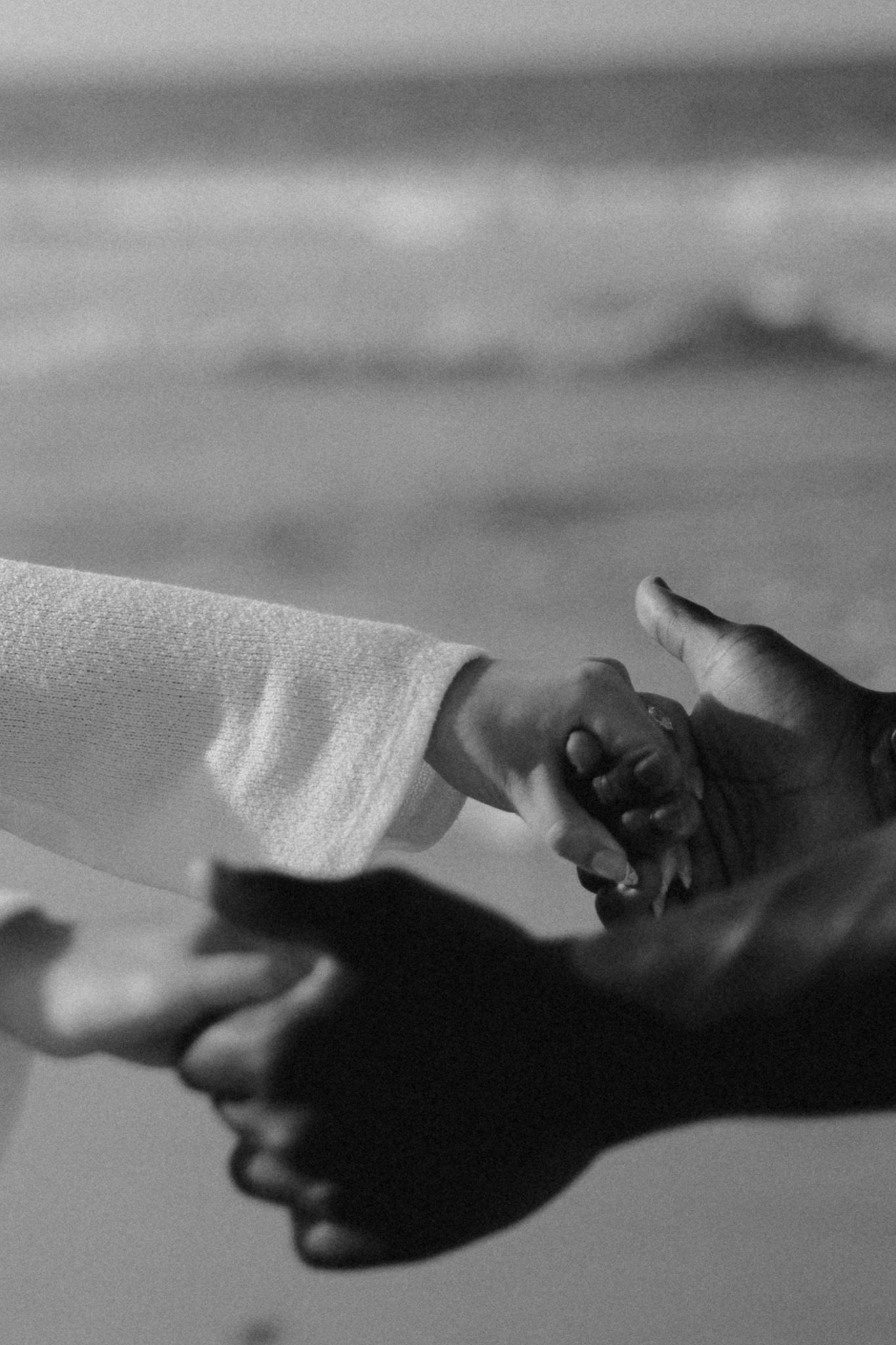 Black and white photo of an adult and child holding hands at the beach, symbolizing love and connection.