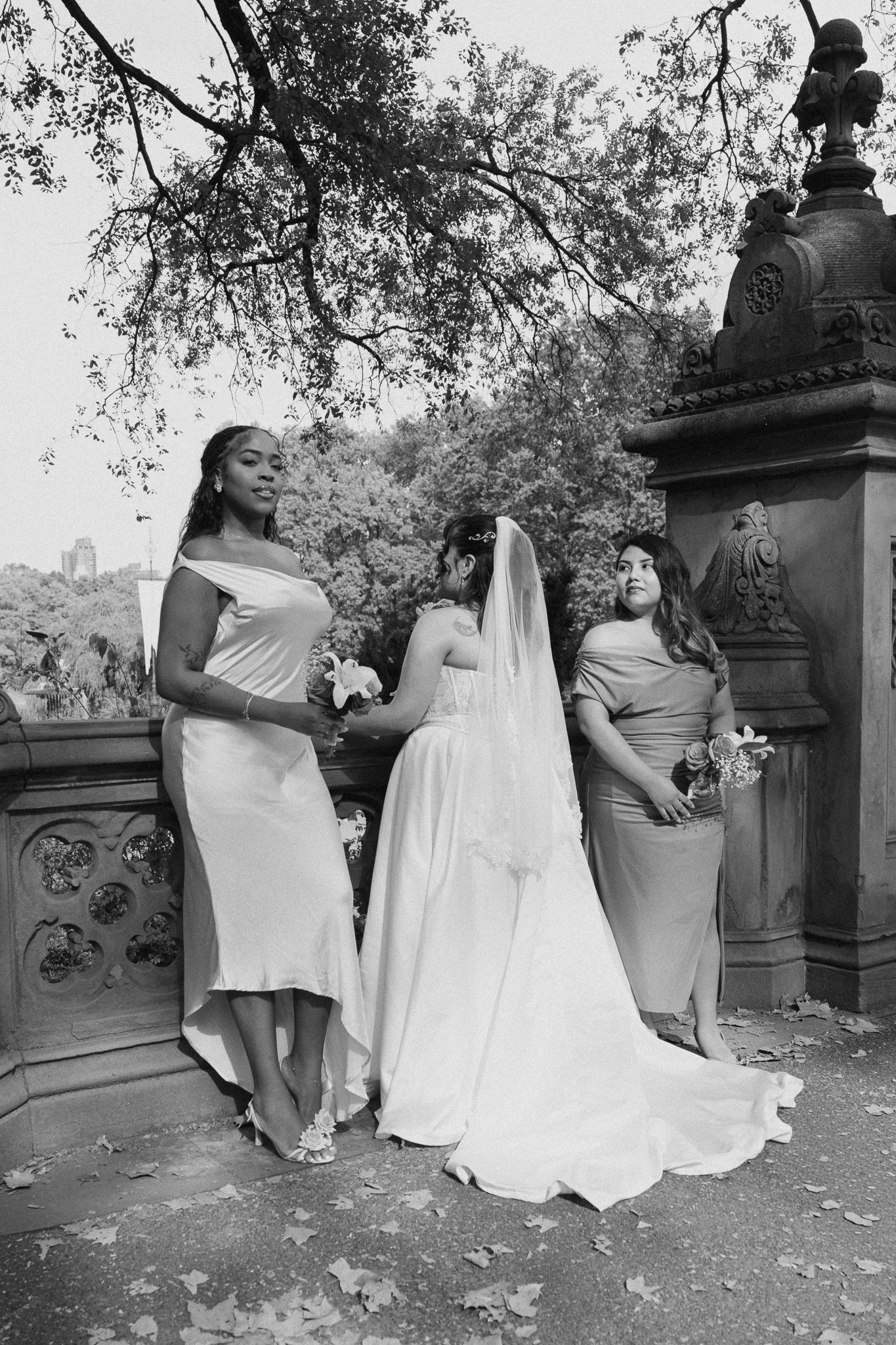 Wedding party in matching off-shoulder dresses poses against stone balustrade in scenic outdoor setting.
