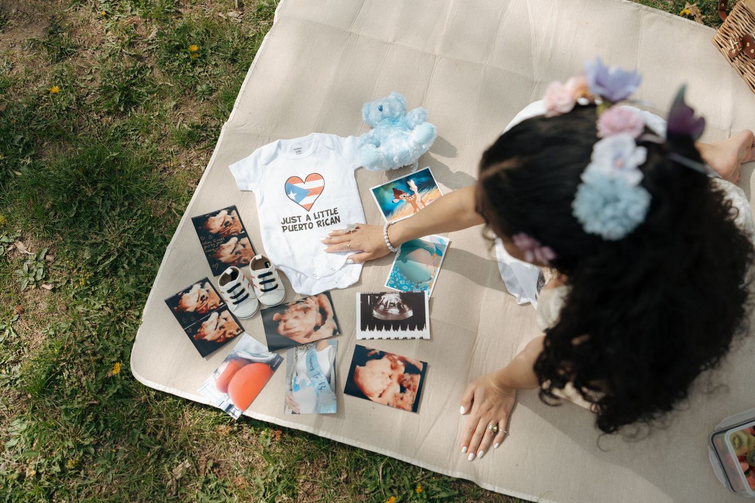 Ultrasound photos and pregnancy memorabilia laid out on a picnic blanket in a park.