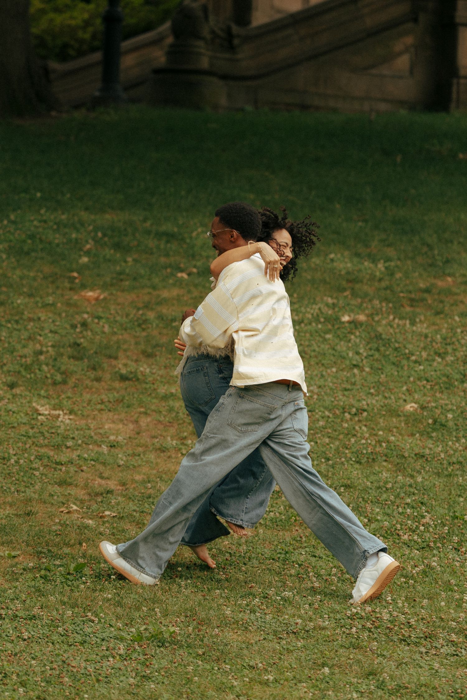 Joyful couple embracing and walking together across a green grassy park lawn.