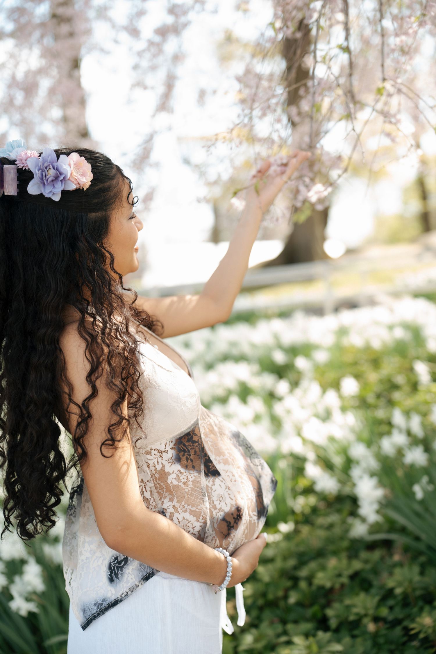 A person in white lace poses gracefully among spring blossoms and trees.