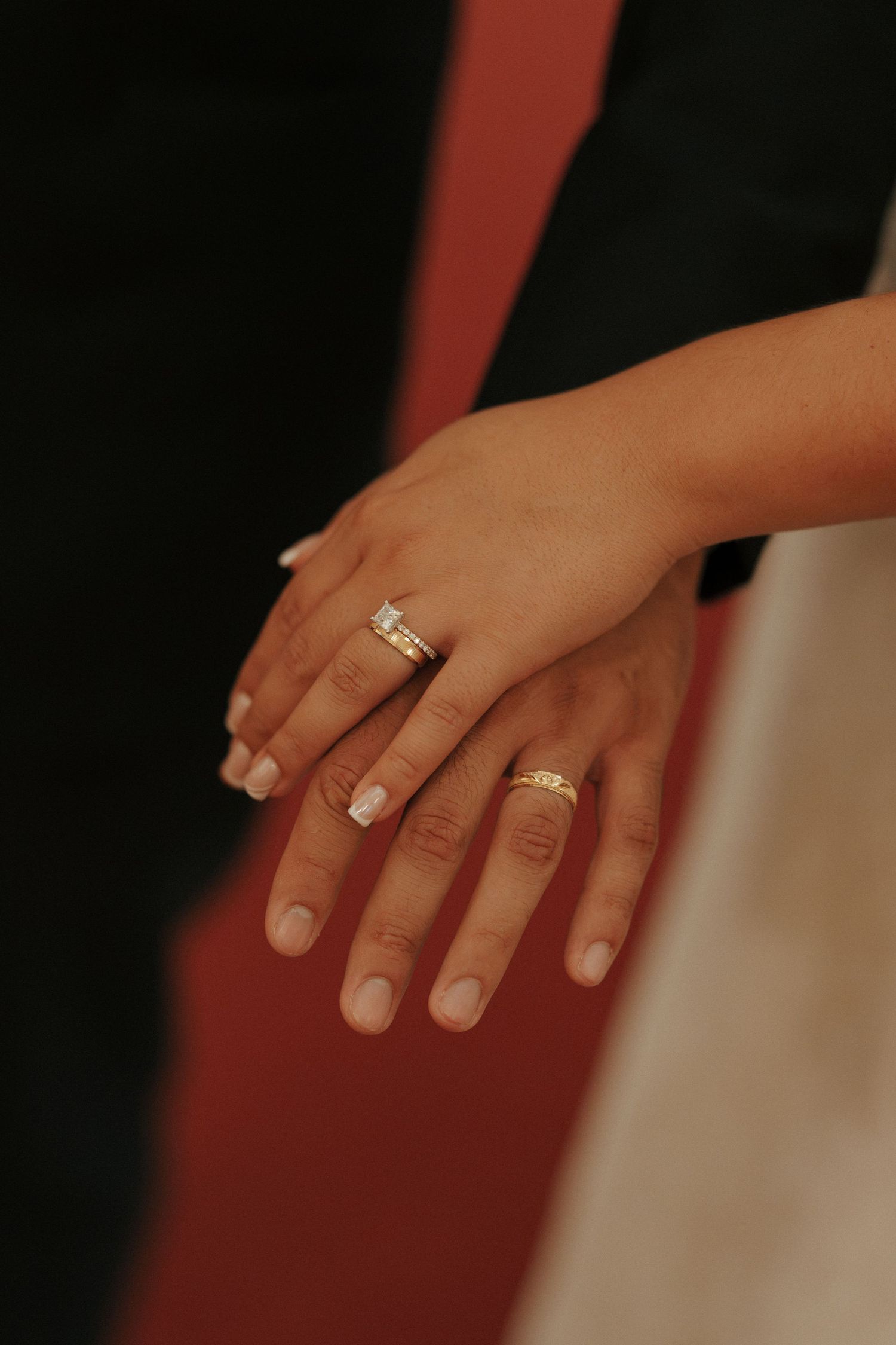 Close-up of two hands displaying wedding rings, one with a diamond engagement ring and one with a gold band.