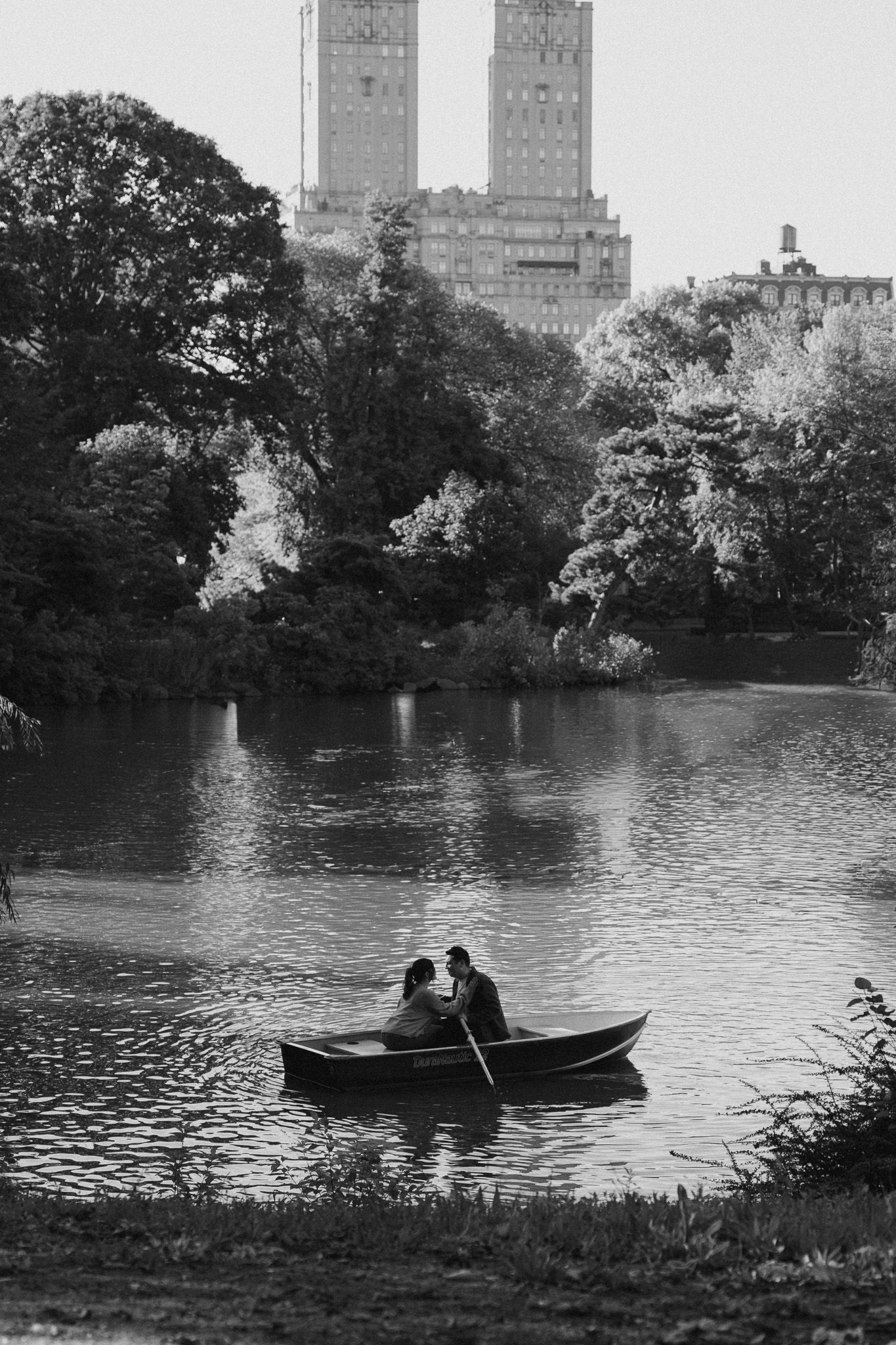 A rowboat glides across a lake in Central Park with Manhattan buildings visible in the background.
