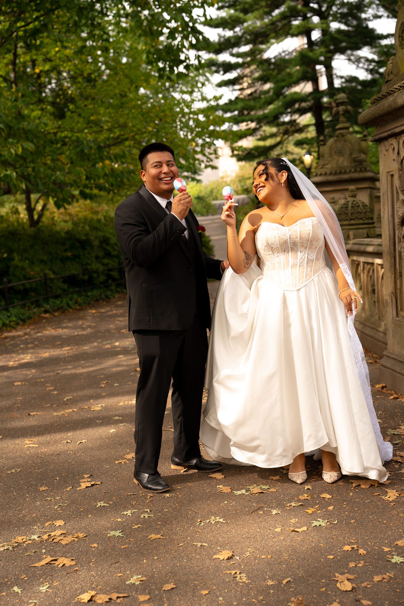 A newlywed couple enjoying ice cream cones together on a tree-lined path.