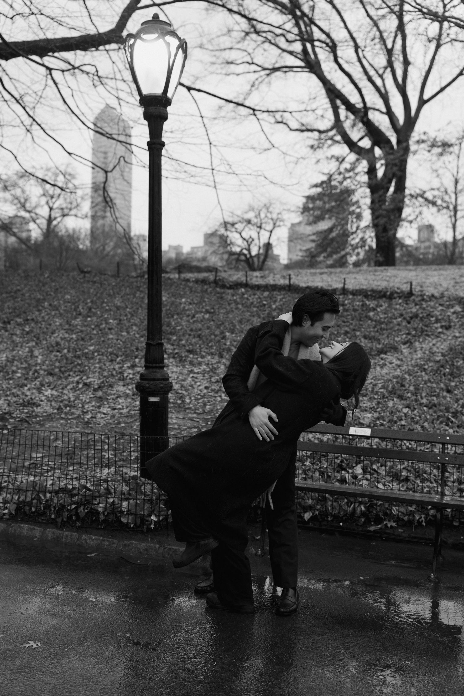 A sequence of black and white photos showing a figure climbing and hanging from a lamppost in a park setting.