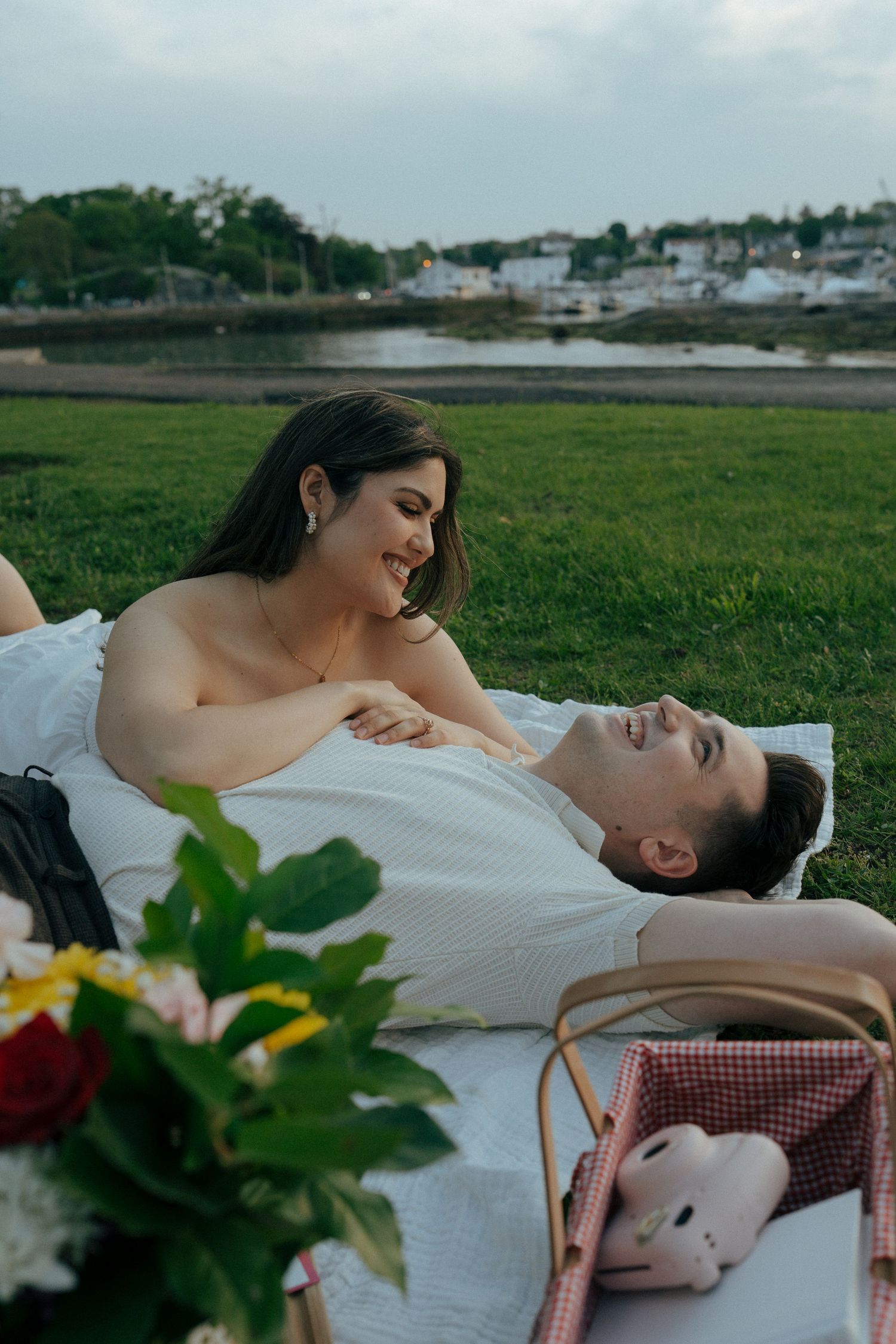 A romantic picnic scene at sunset with a couple lying on a blanket in a grassy field.