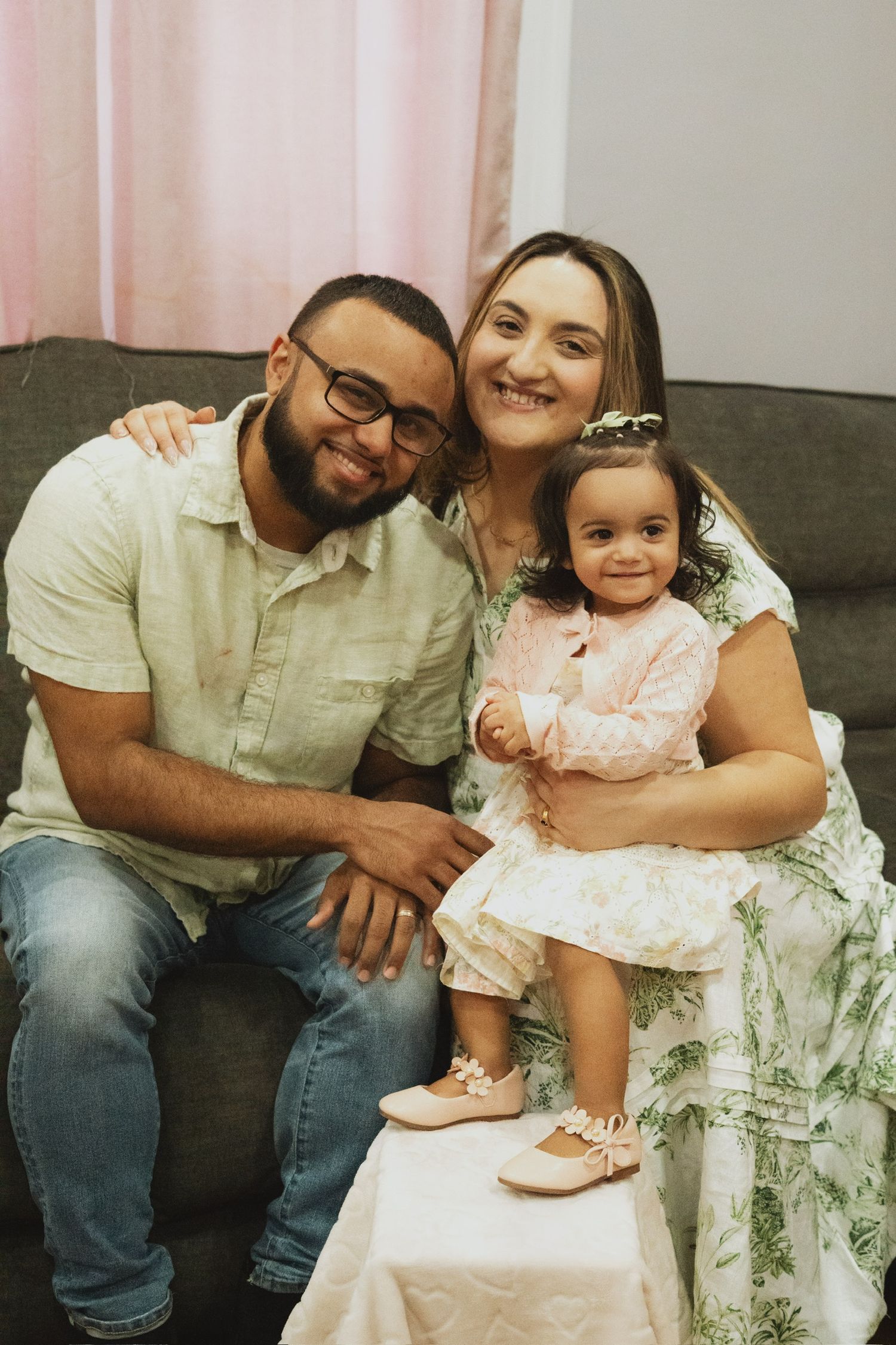 A family sits together on a pink chair for a casual indoor portrait.