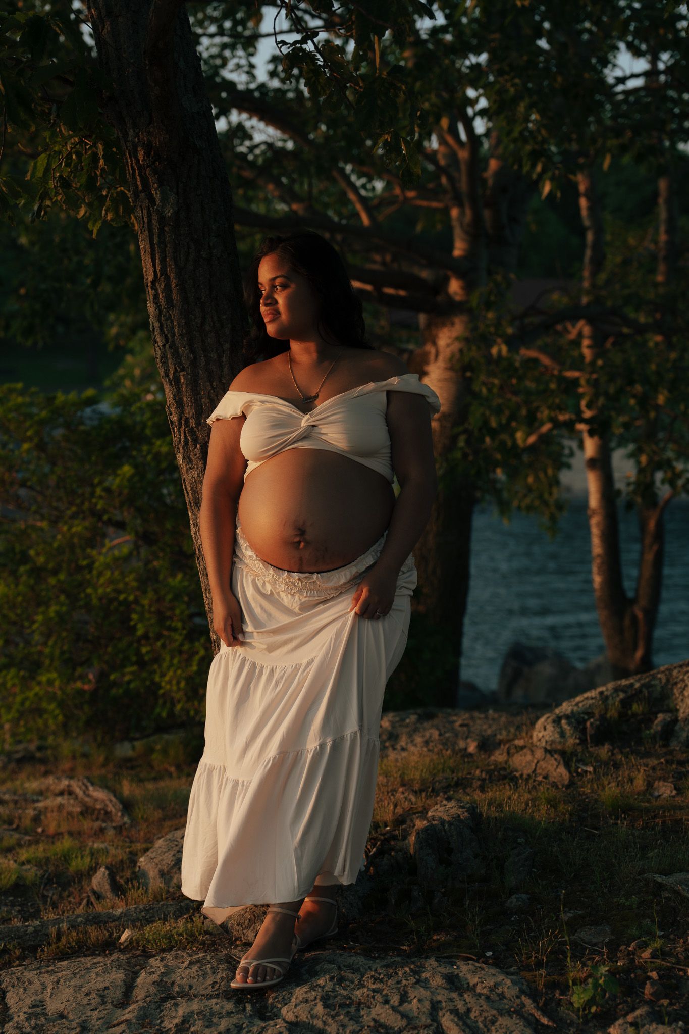 Person in white dress posing on rocky coastline during sunset.