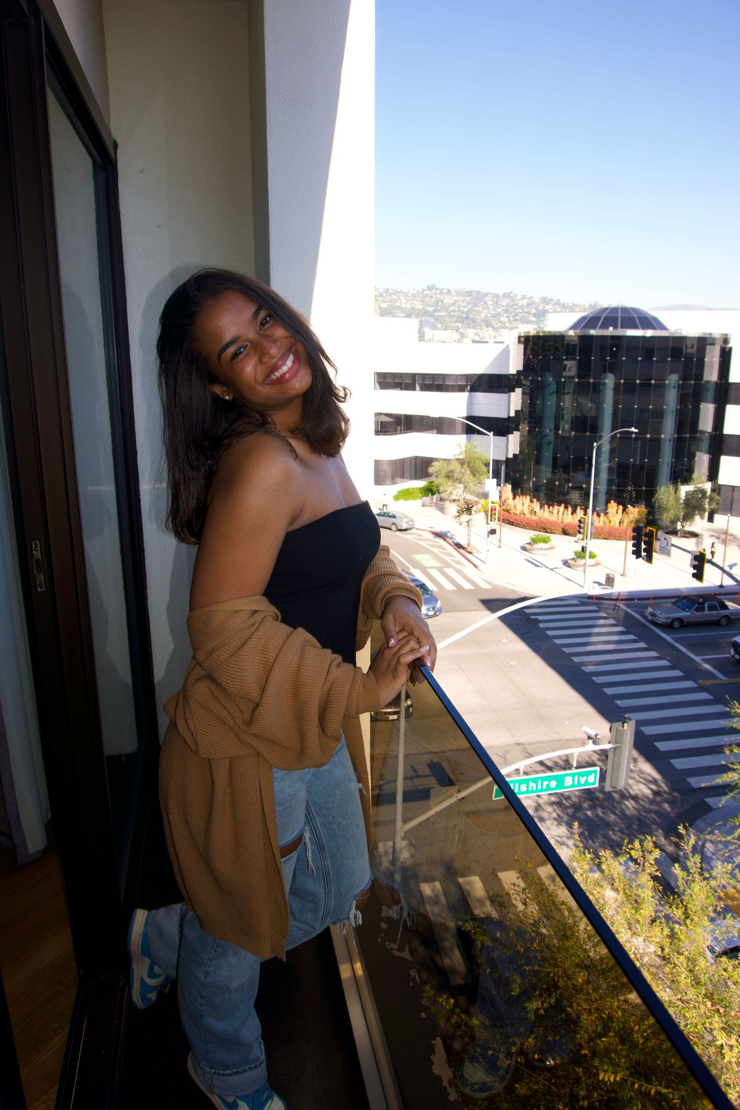 A sequence of photos showing someone posing and smiling on an outdoor balcony with city views in the background.