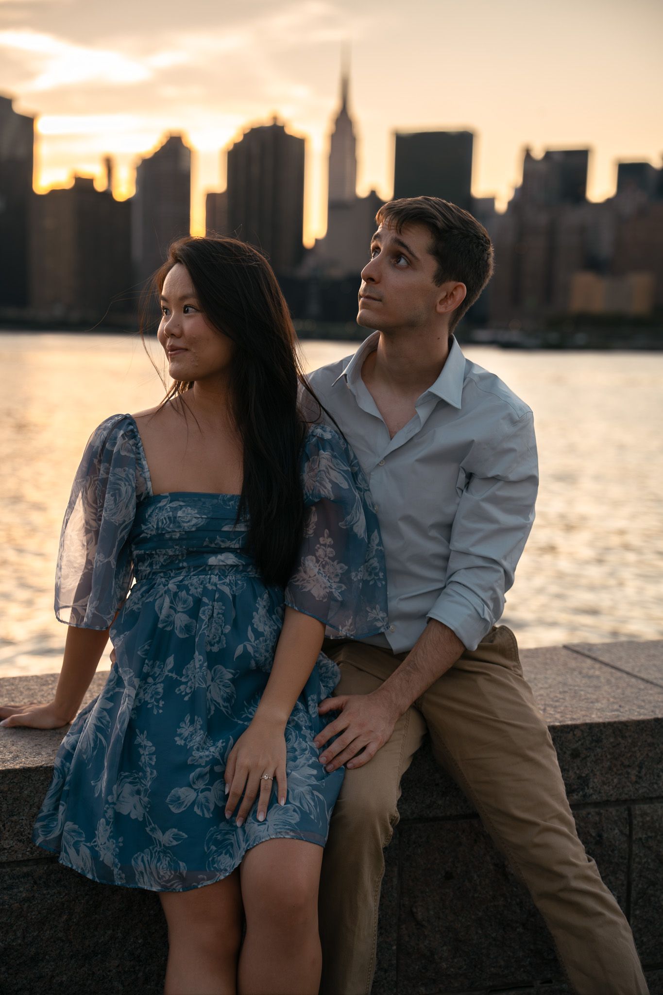 Couple sitting together by the waterfront with NYC skyline silhouetted at sunset.
