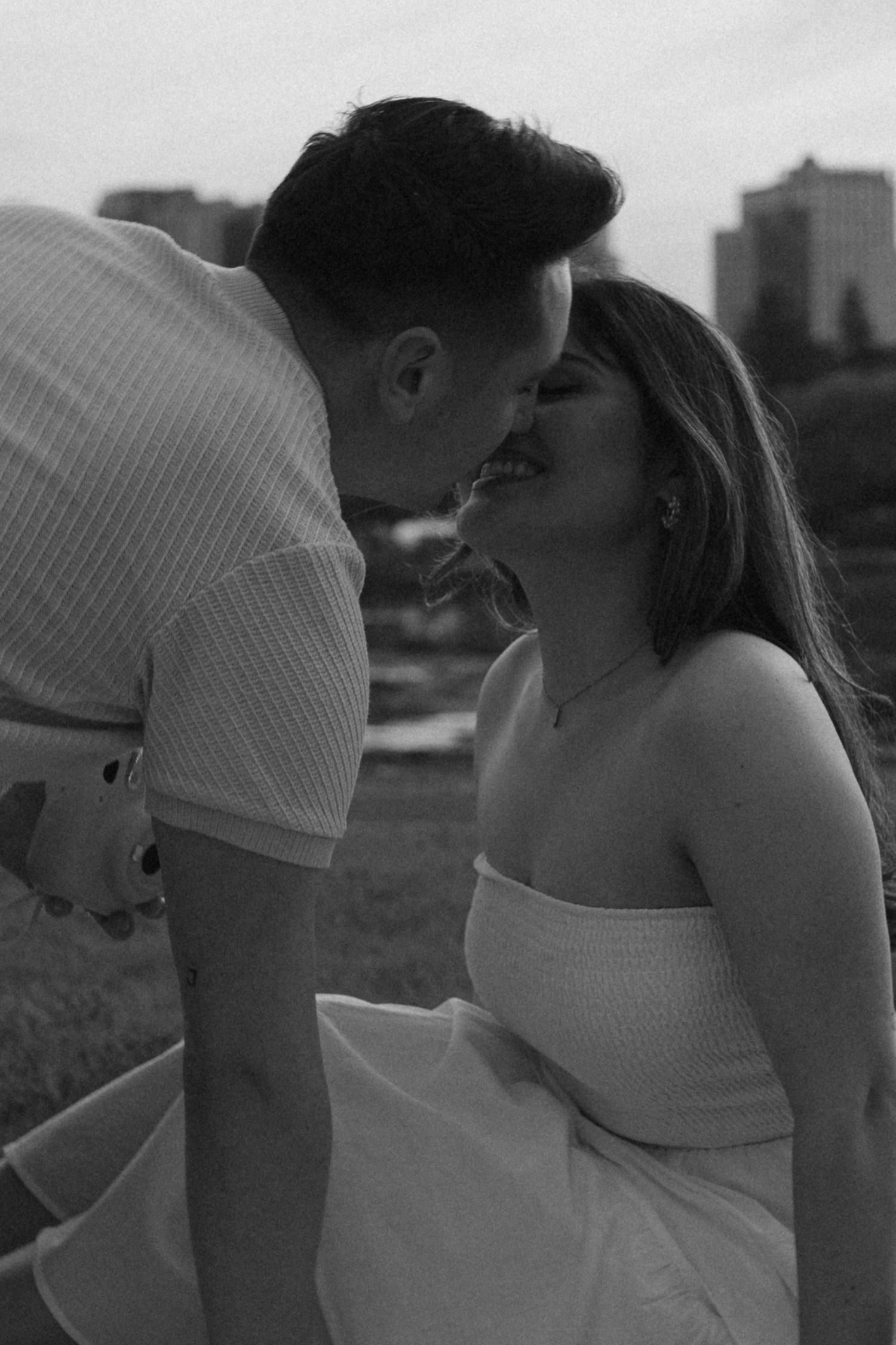 Black and white romantic portrait with city skyline in background.