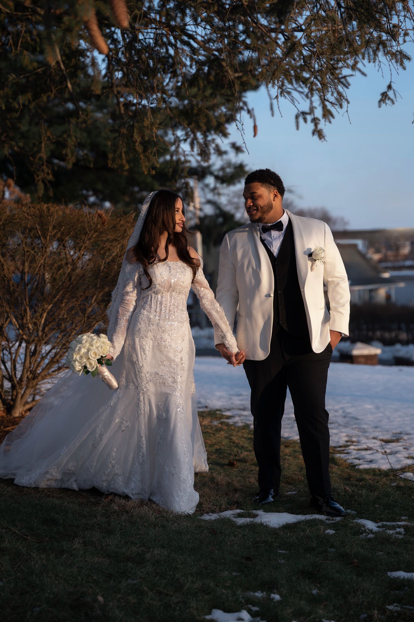 A couple in wedding attire poses together in a snowy winter landscape at sunset, creating a romantic silhouette effect.