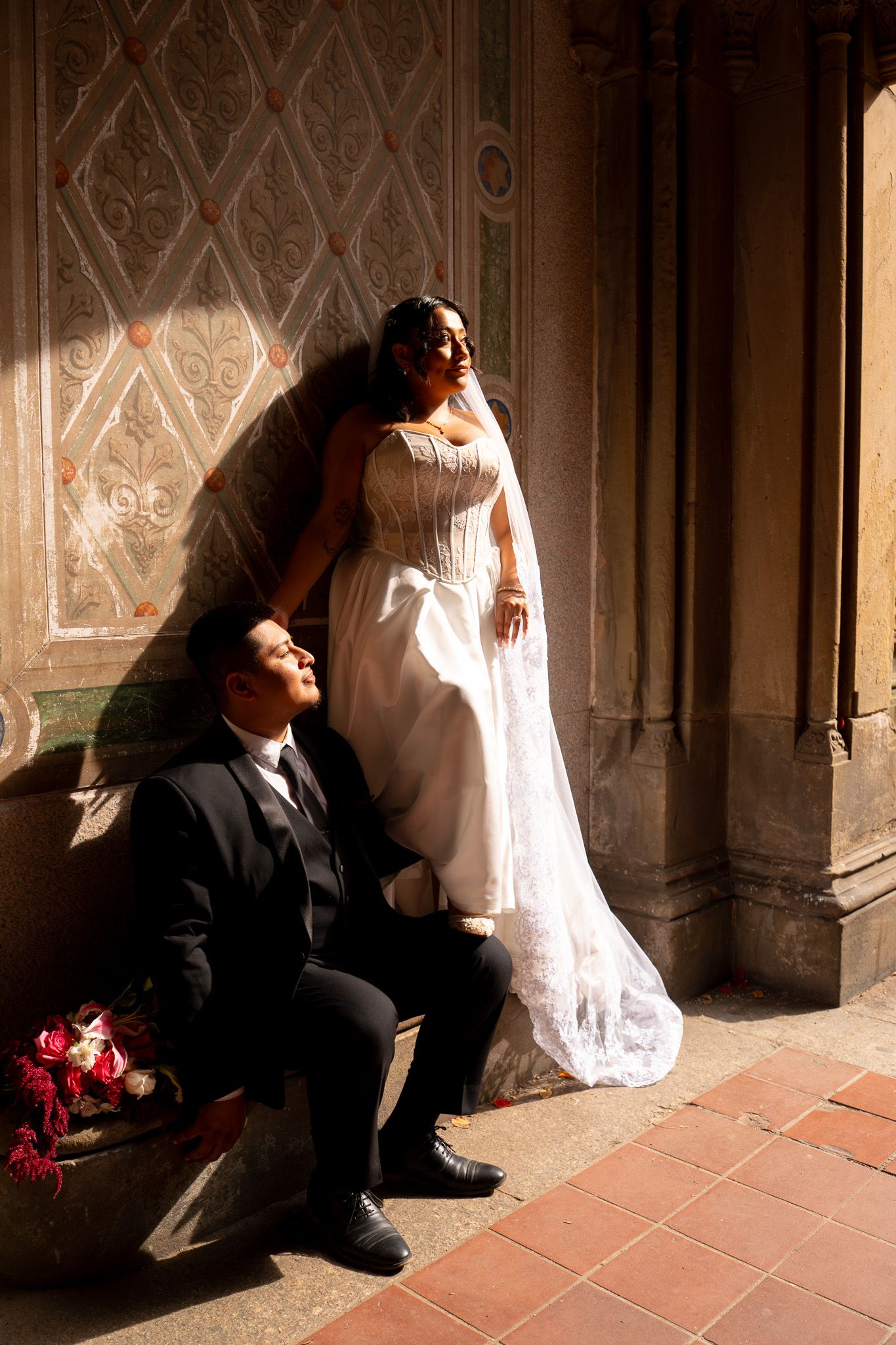 A dramatic wedding portrait with natural window light streaming through an ornate archway.