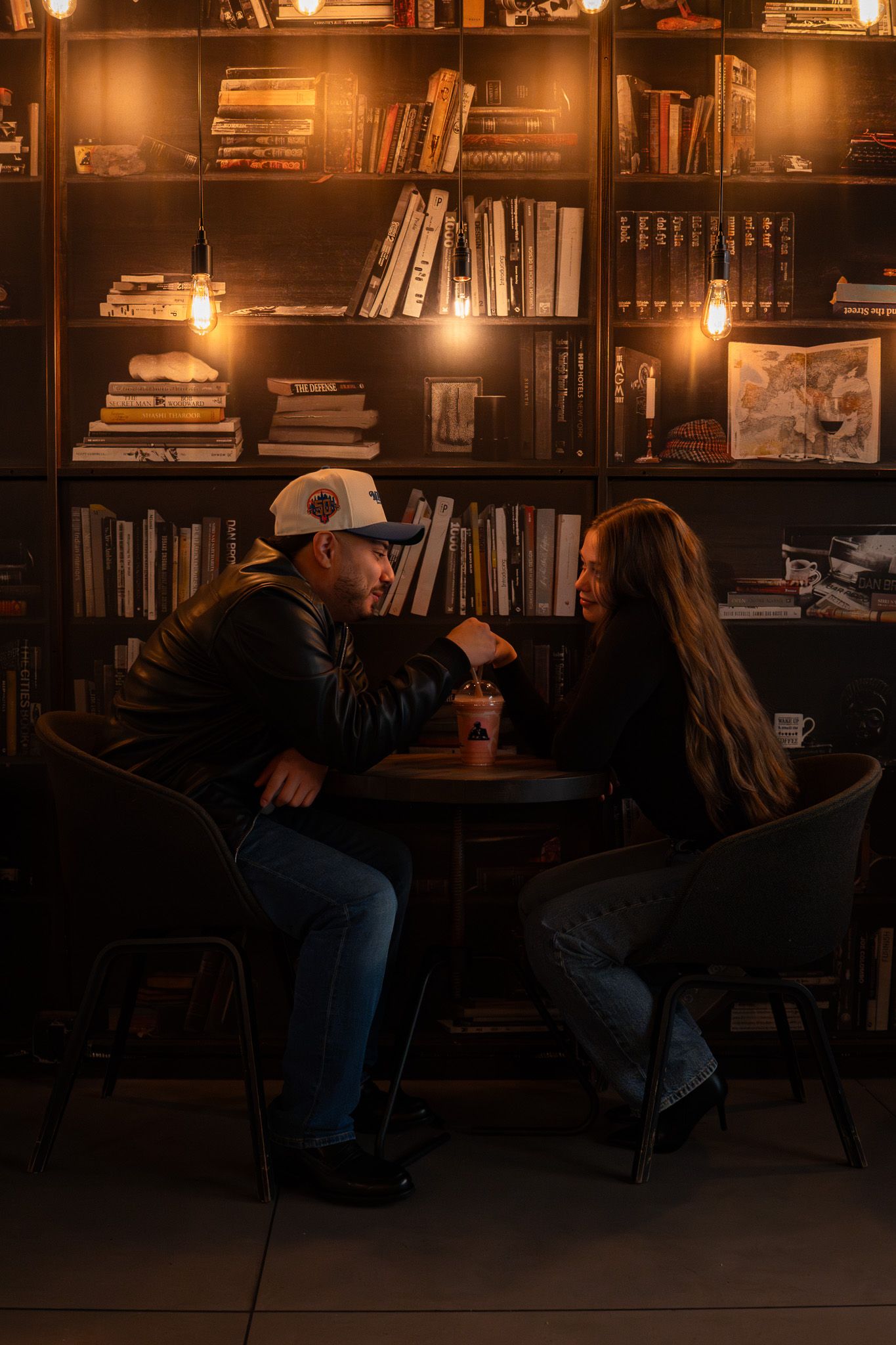Two people sit together in a cozy library setting illuminated by warm lighting.