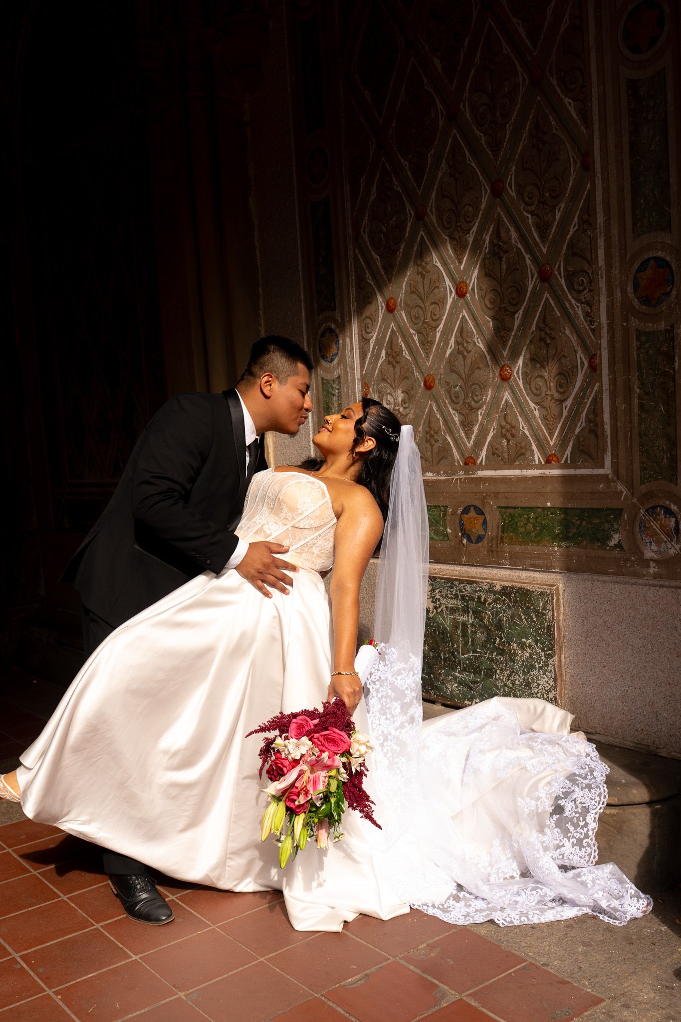A romantic wedding portrait with a beautiful bouquet against an ornate architectural backdrop.