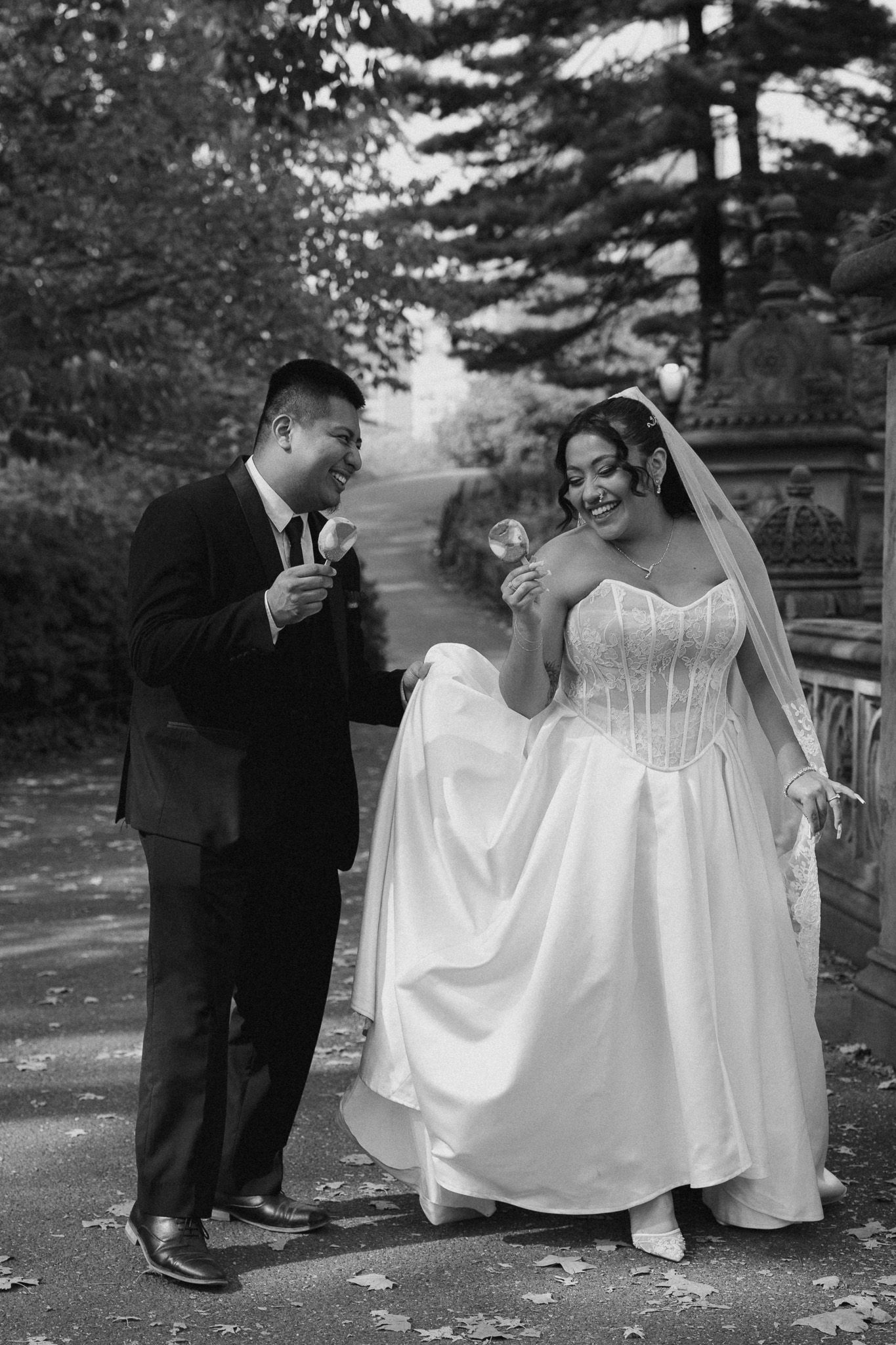 A black and white wedding photo of a couple sharing a playful moment on a garden path.