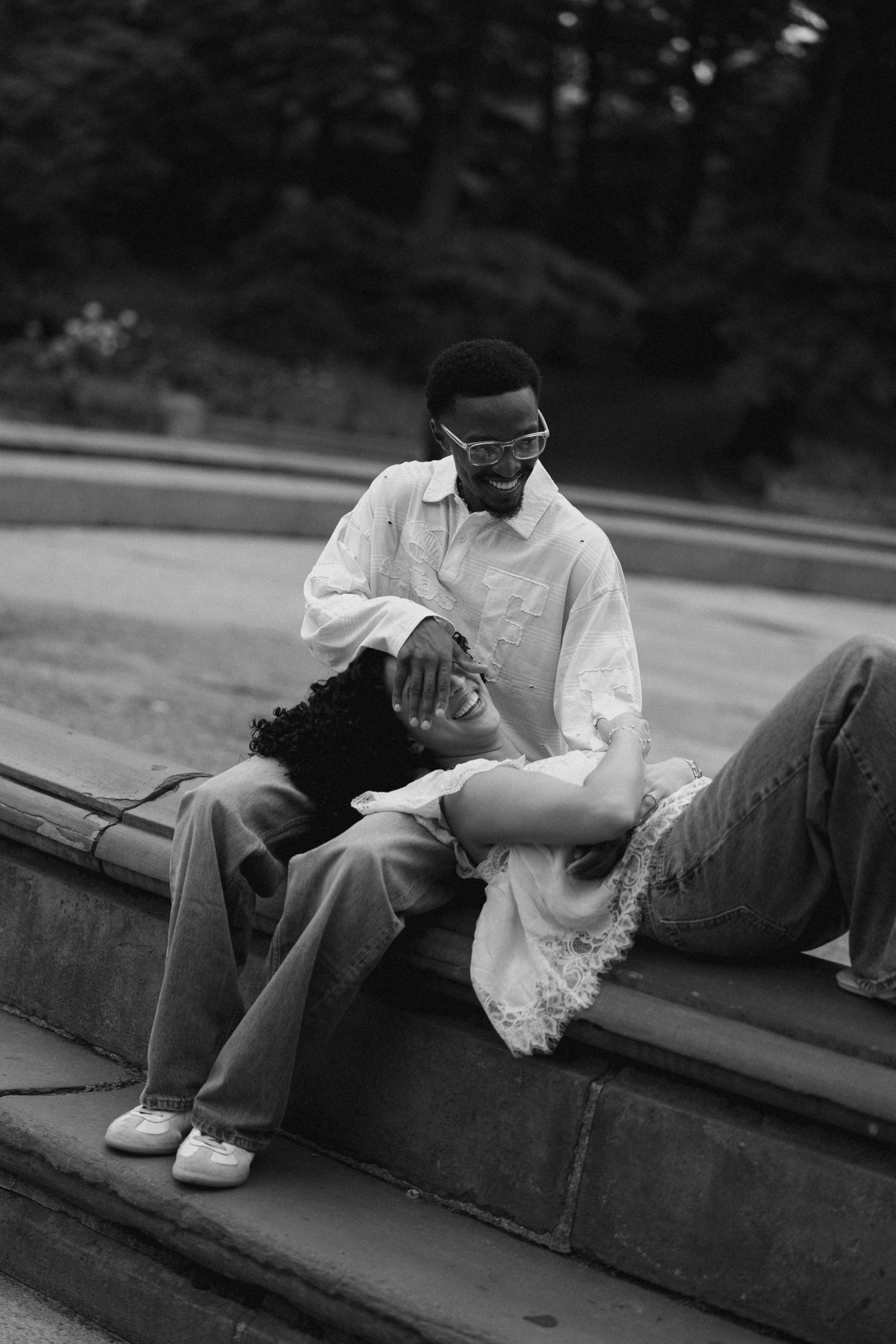 Black and white photo of a couple relaxing on steps, woman lying in mans lap, both smiling.