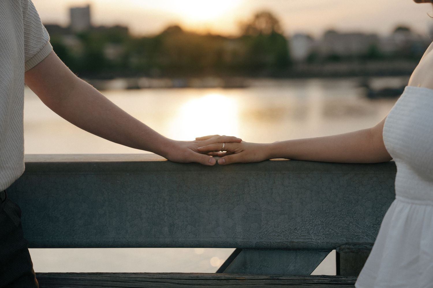 A couple holding hands against a sunset waterfront backdrop.