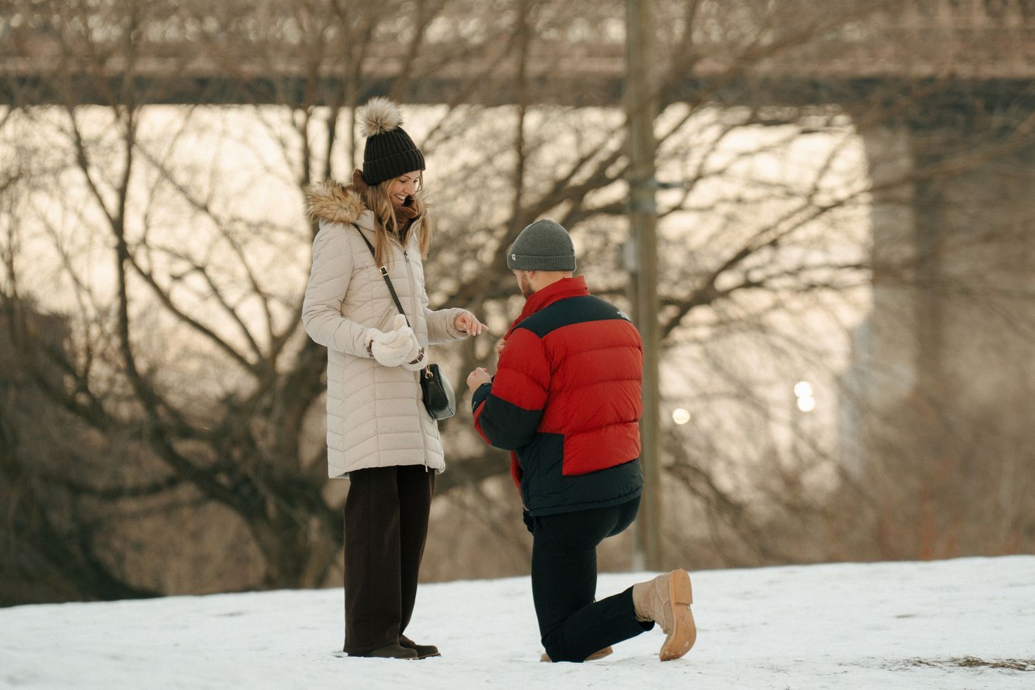 A couple in winter coats shares a special moment during a snowy outdoor proposal.