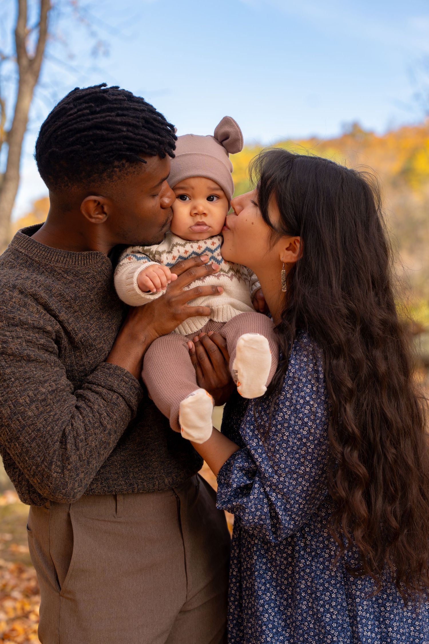 A loving family shares tender kisses together during an autumn photoshoot with golden trees in the background.