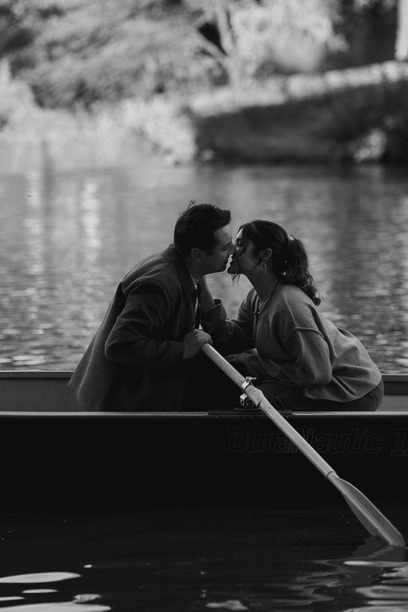 A romantic scene of two people in a rowboat on calm waters in black and white.