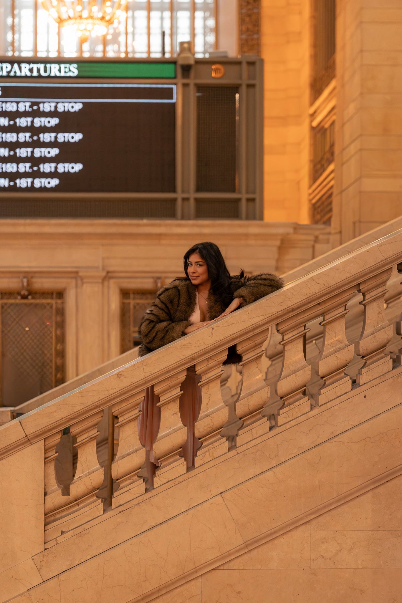 Person sits on marble staircase in Grand Central Terminal's warm-lit interior with departure board visible above.